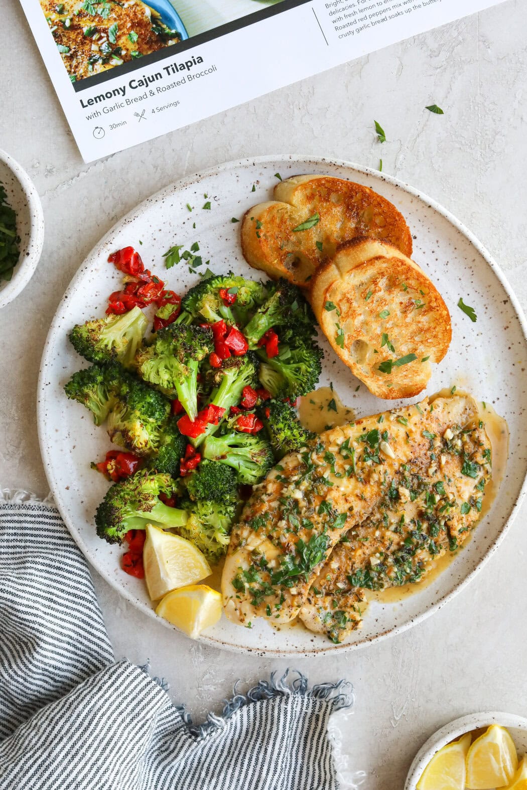 Overhead view of a plate of chicken, garlic bread, and roasted vegetables topped with fresh herbs. 