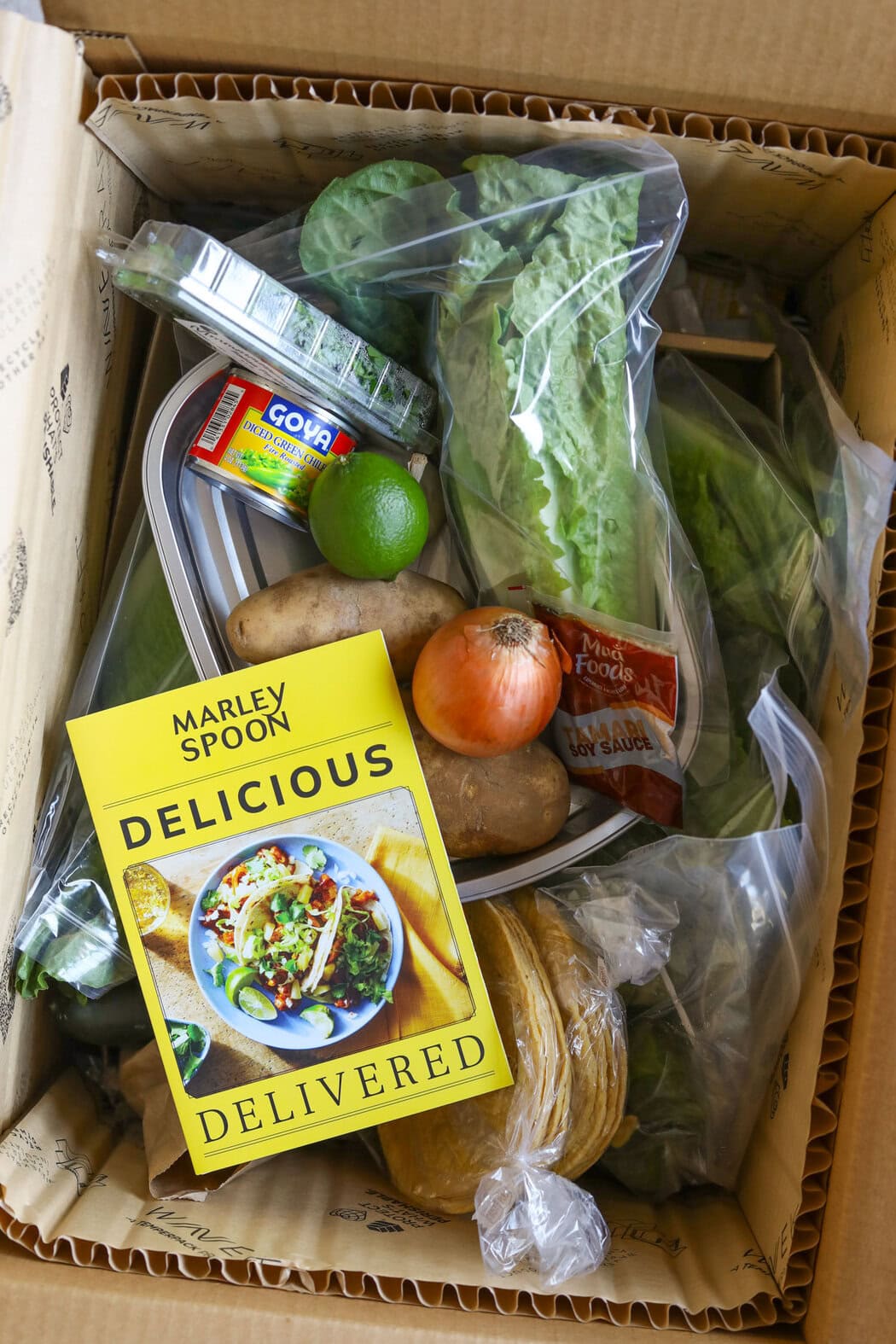 Overhead view of a box of Marley Spoon delivery food ingredients and a recipe book. 