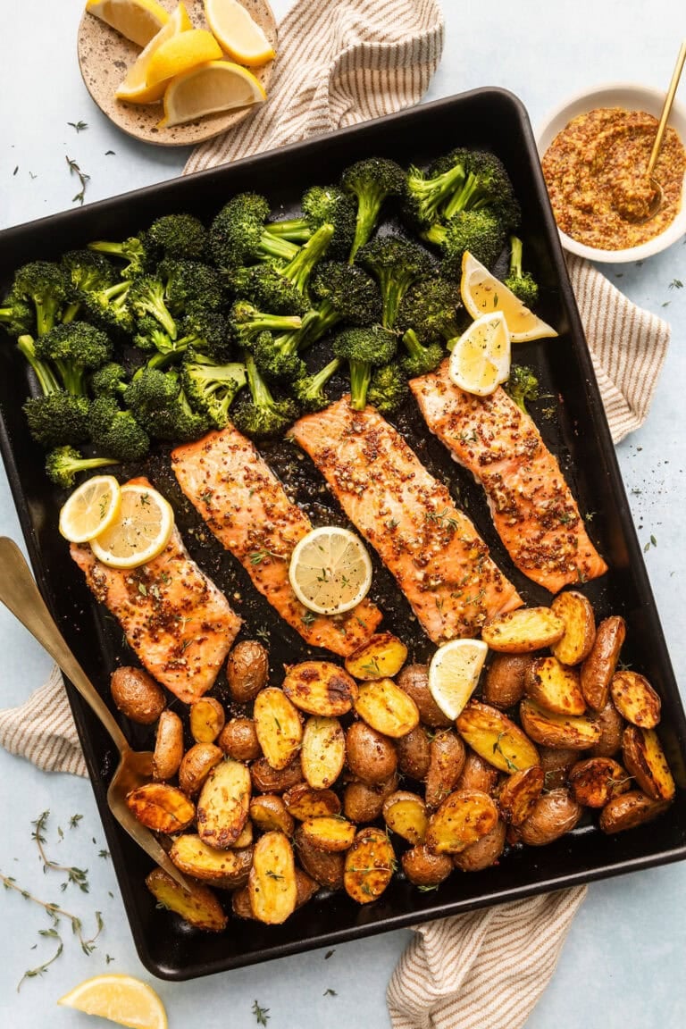 Overhead view of a sheet pan filled with honey mustard salmon and broccoli and potatoes garnished with lemon wedges. 