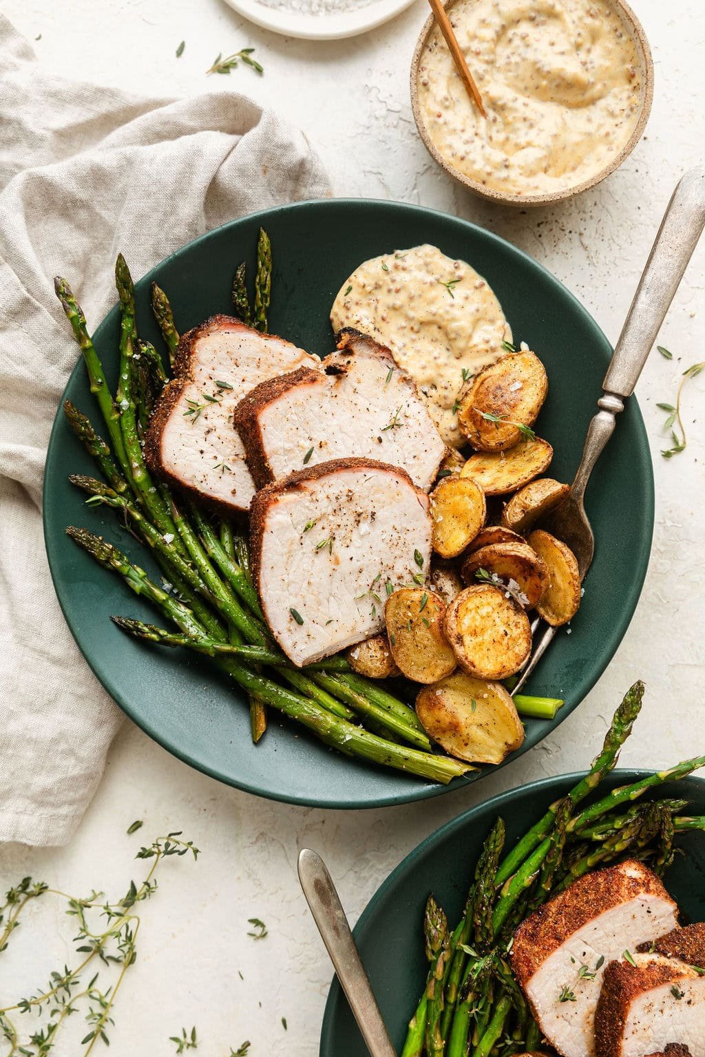 Overhead view of a plate of Sheet Pan Pork Tenderloin with potatoes and asparagus next to a homemade aioli dipping sauce. 