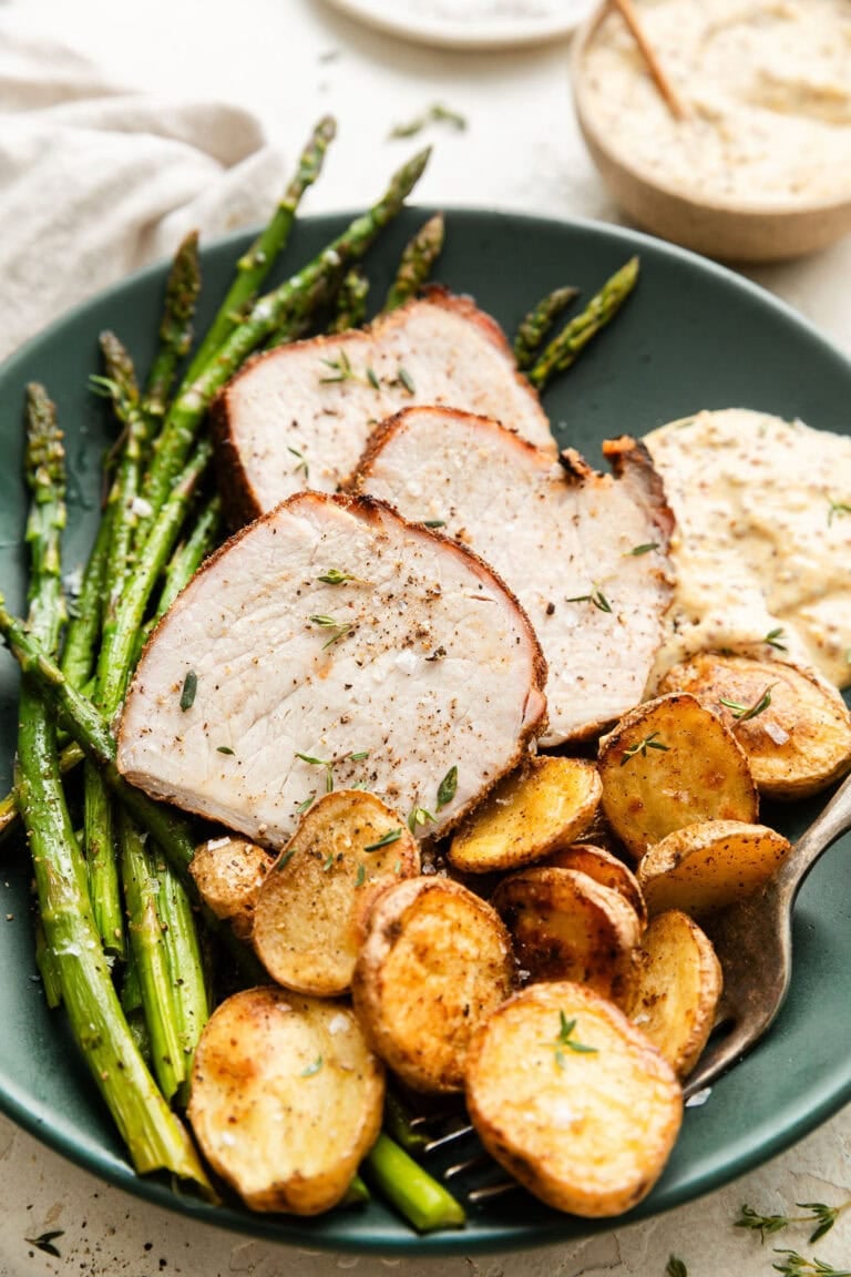 A plate of sliced pork tenderloin with potatoes, asparagus, and a 2-ingredient creamy mustard dipping sauce