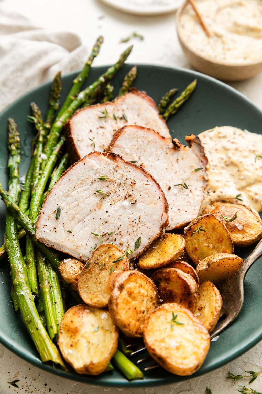 Overhead view of a plate of freshly roasted Sheet Pan Pork Tenderloin with potatoes and asparagus topped with fresh herbs and seasonings. 