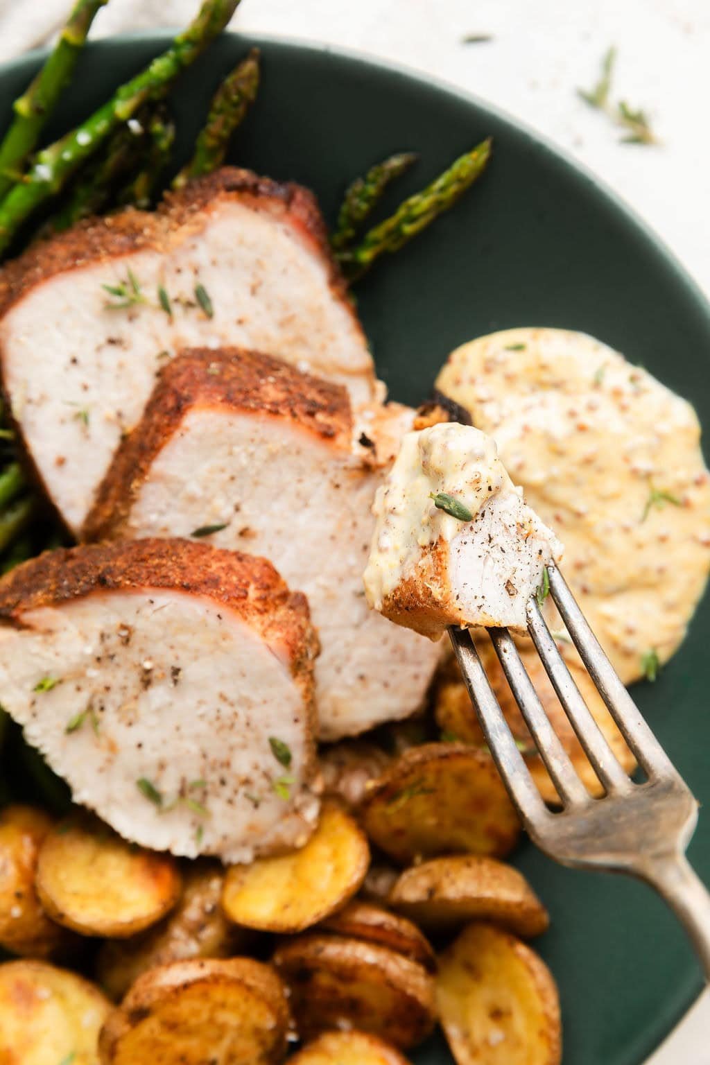 Close up view of a fork holding a bite of Sheet Pan Pork Tenderloin dipped in the aioli sauce. 