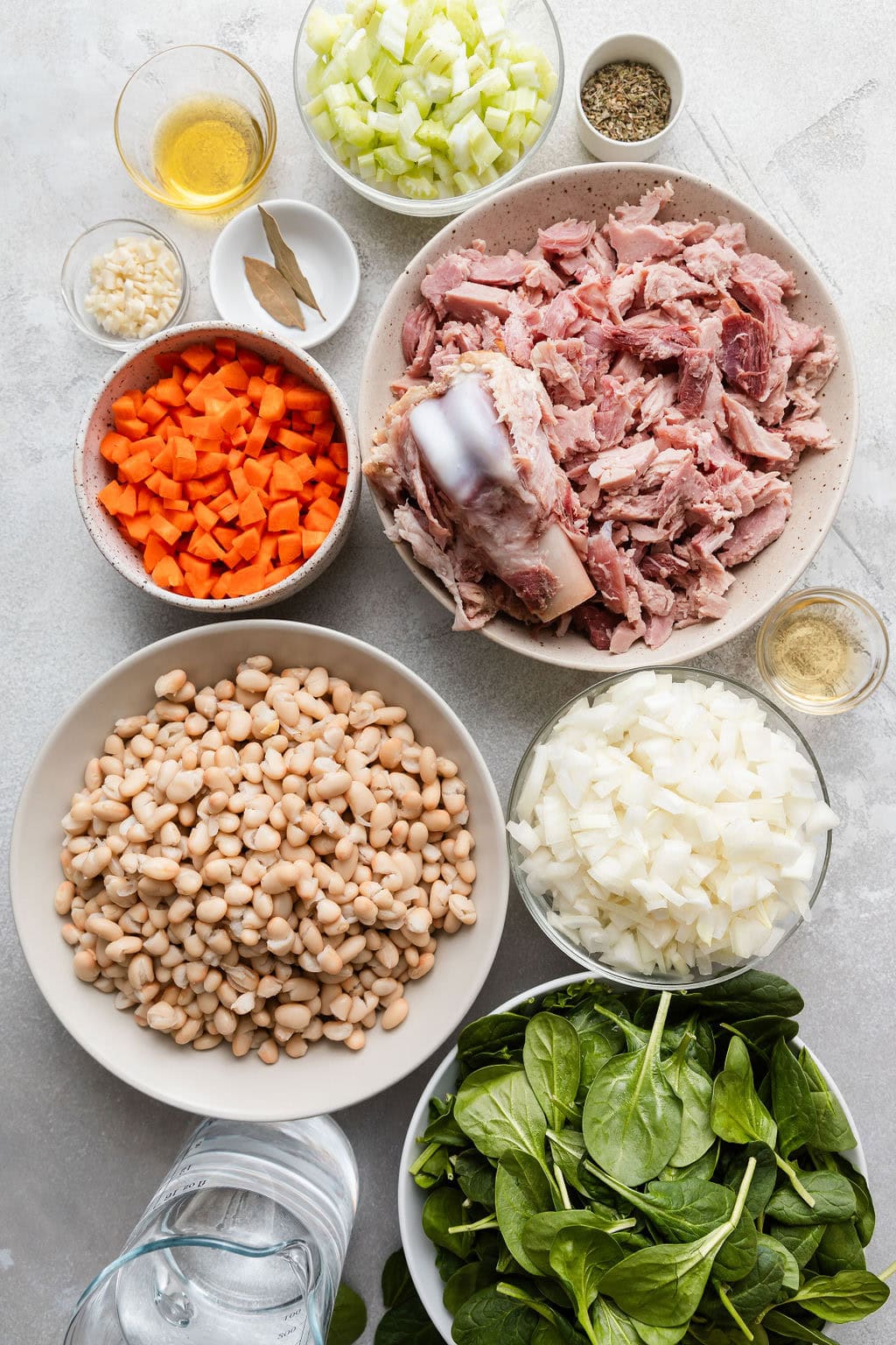Overhead view of a variety of ingredients for Ham And Bean Soup in different sized bowls.