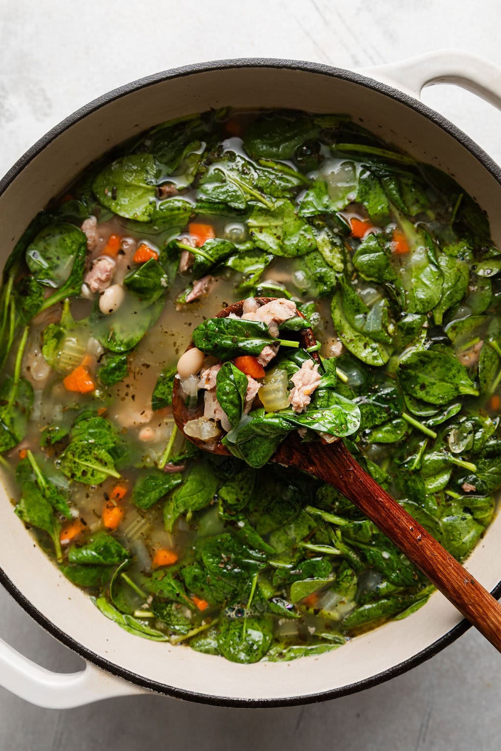 Overhead view of a Dutch oven filled with Ham and Bean Soup ingredients being stirred with a wooden spoon. 