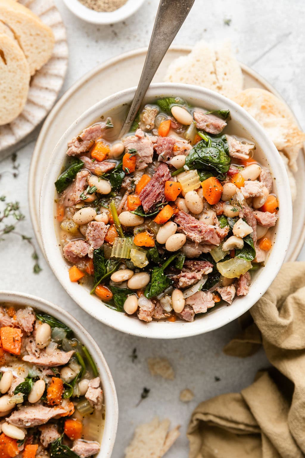 Overhead view of 2 bowls of Ham and Bean Soup with bread pieces on the side. 
