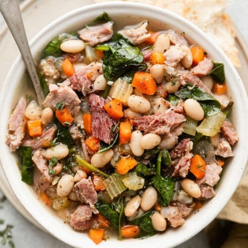 Close up view of bean and ham soup in a white bowl.