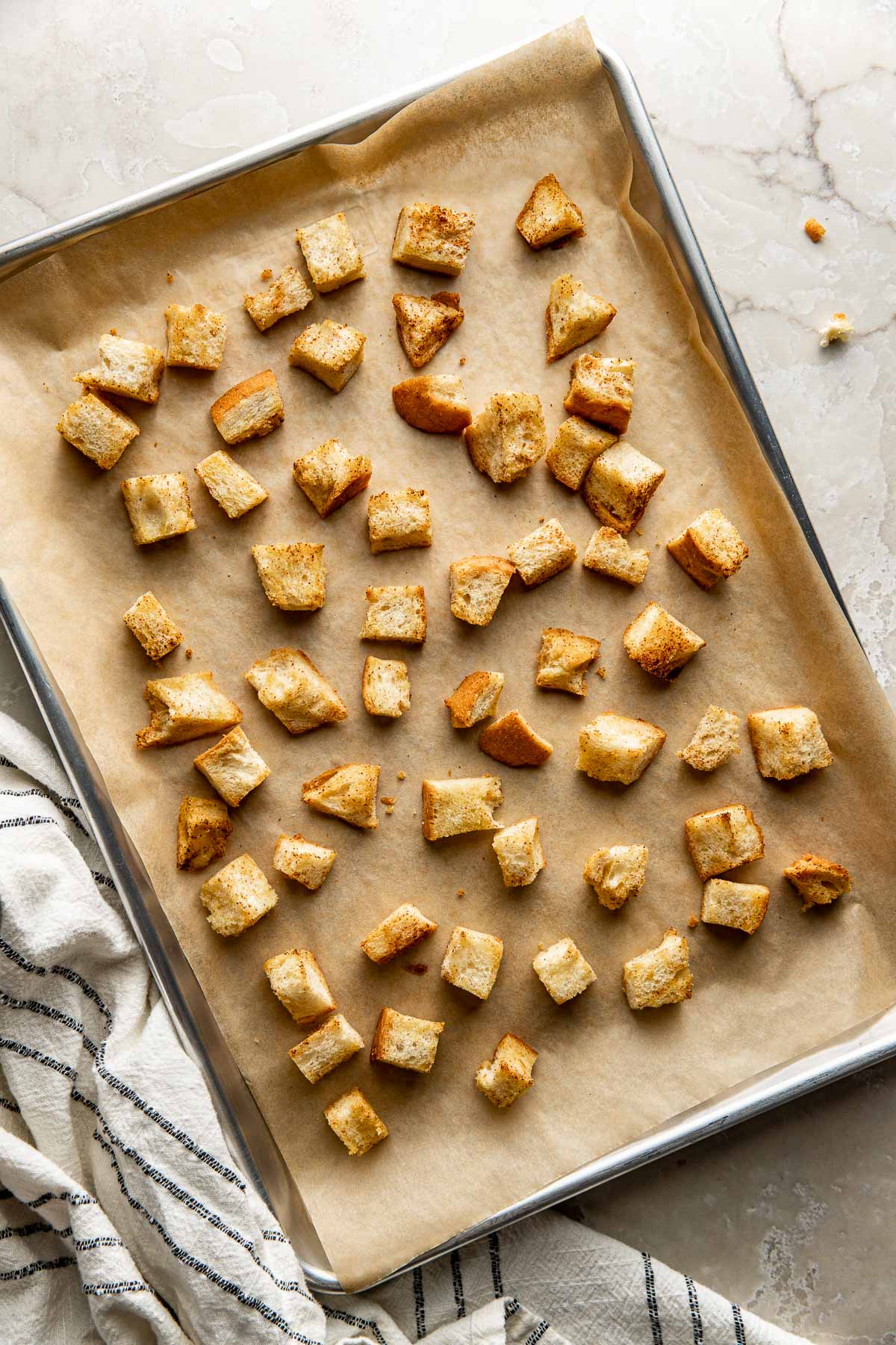 Overhead view of a sheet pan of Homemade Croutons freshly baked and crisp on the edges. 