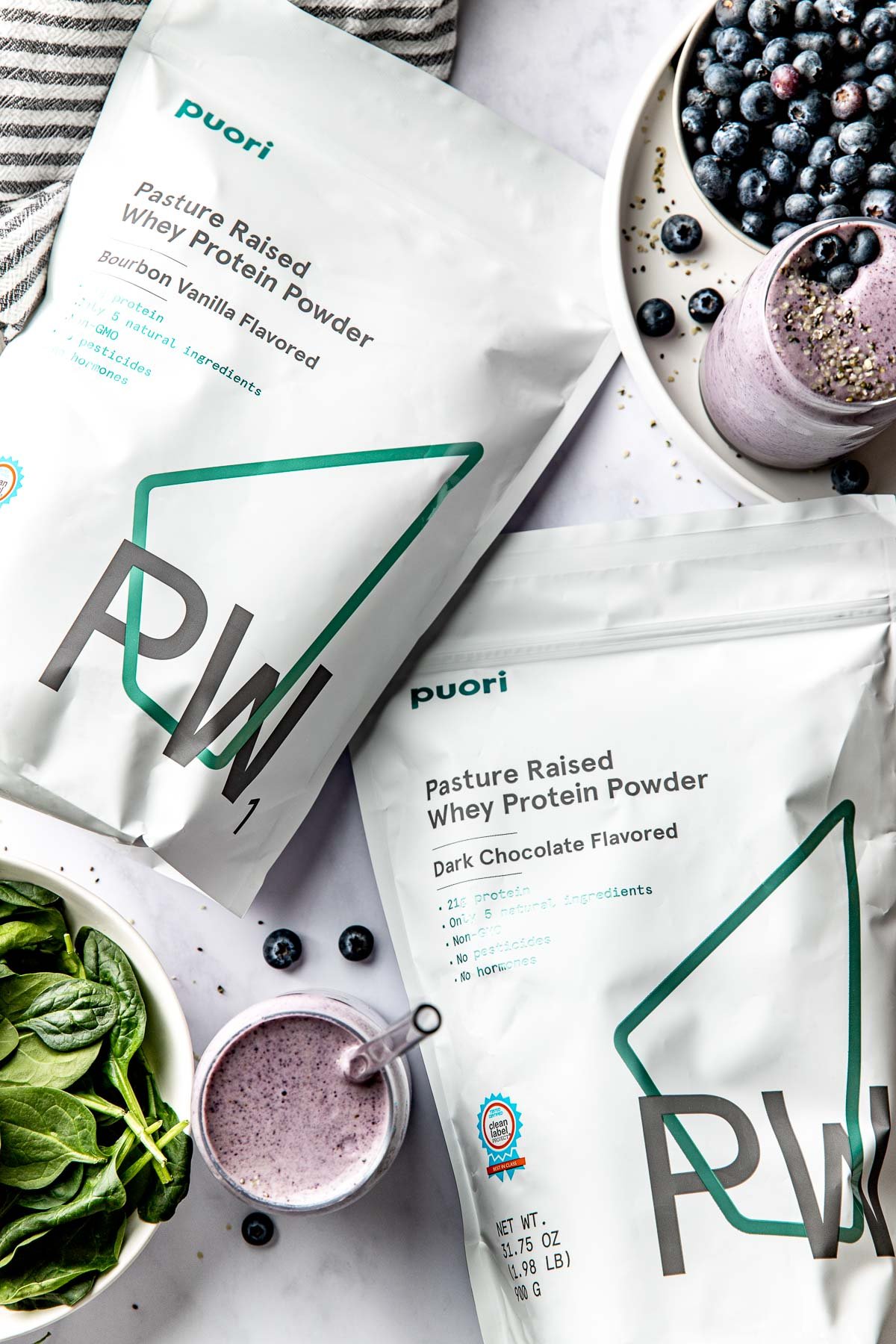 Overhead view of two bags of Puori protein powder surrounded by hemp seeds and smoothie ingredients. 