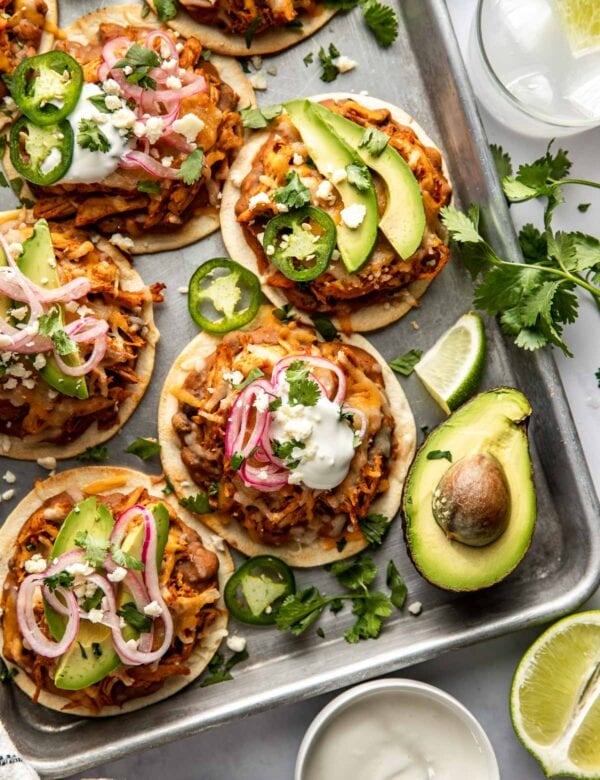 Overhead view chicken tostadas topped with melted cheese, pickles onions, and avocado slices; on a sheet pan.