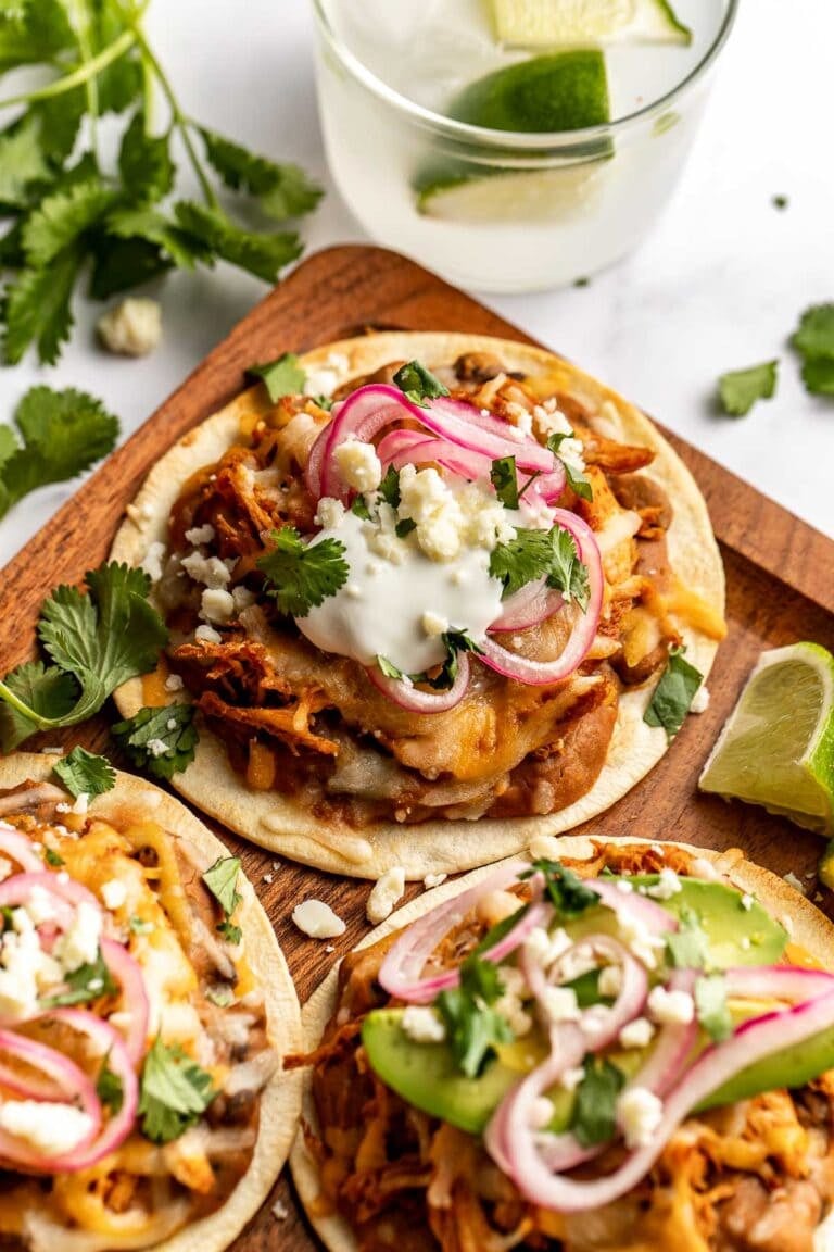 Overhead view of a wooden cutting board filled with chicken tostadas topped with sour cream and fresh cilantro. 
