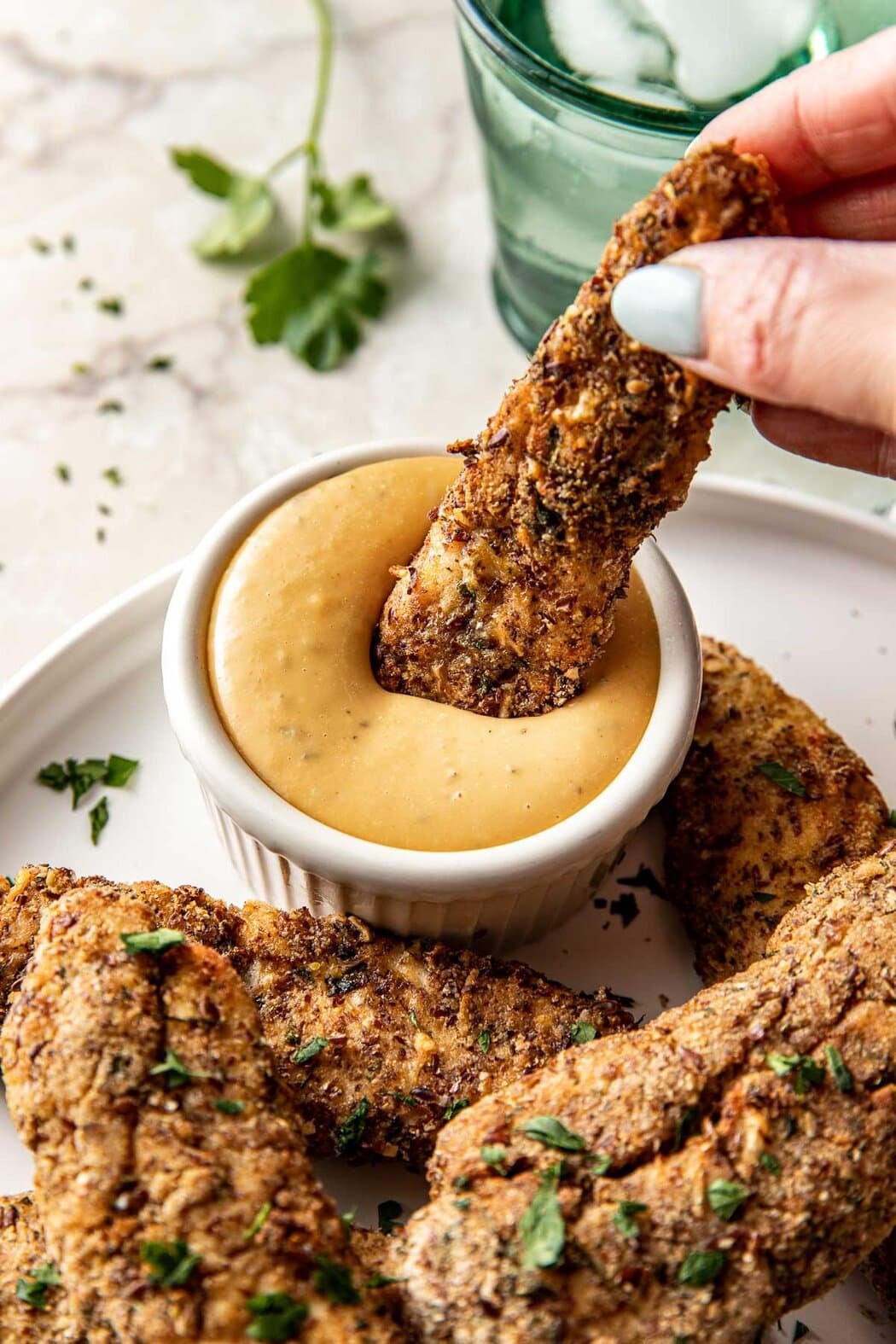 Close up view of a hand holding an Air Fryer Chicken Tender and dipping it into a small bowl of honey mustard sauce. 
