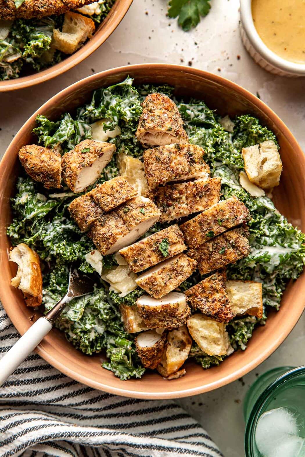Close up view of a kale Caesar salad topped with croutons and sliced Air Fryer Chicken Tenders topped with fresh herbs and flakey sea salt. 