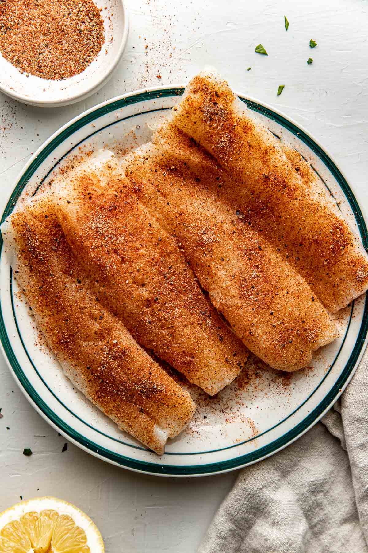 Overhead view of seasoned cod on a plate ready for baking. 