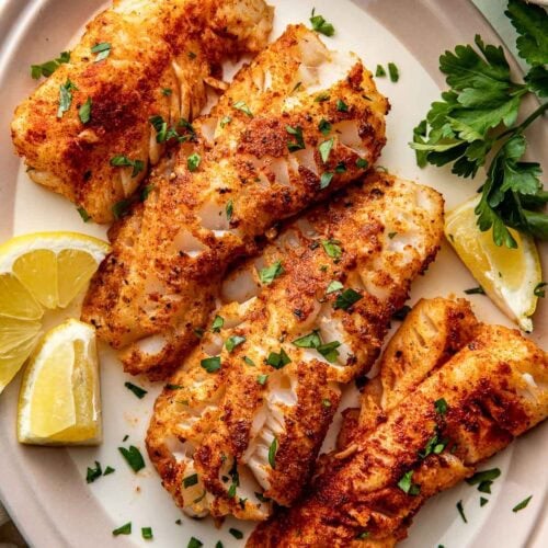 Overhead view of Air Fryer Cod strips on a plate topped with fresh herbs and garnished with lemon wedges.