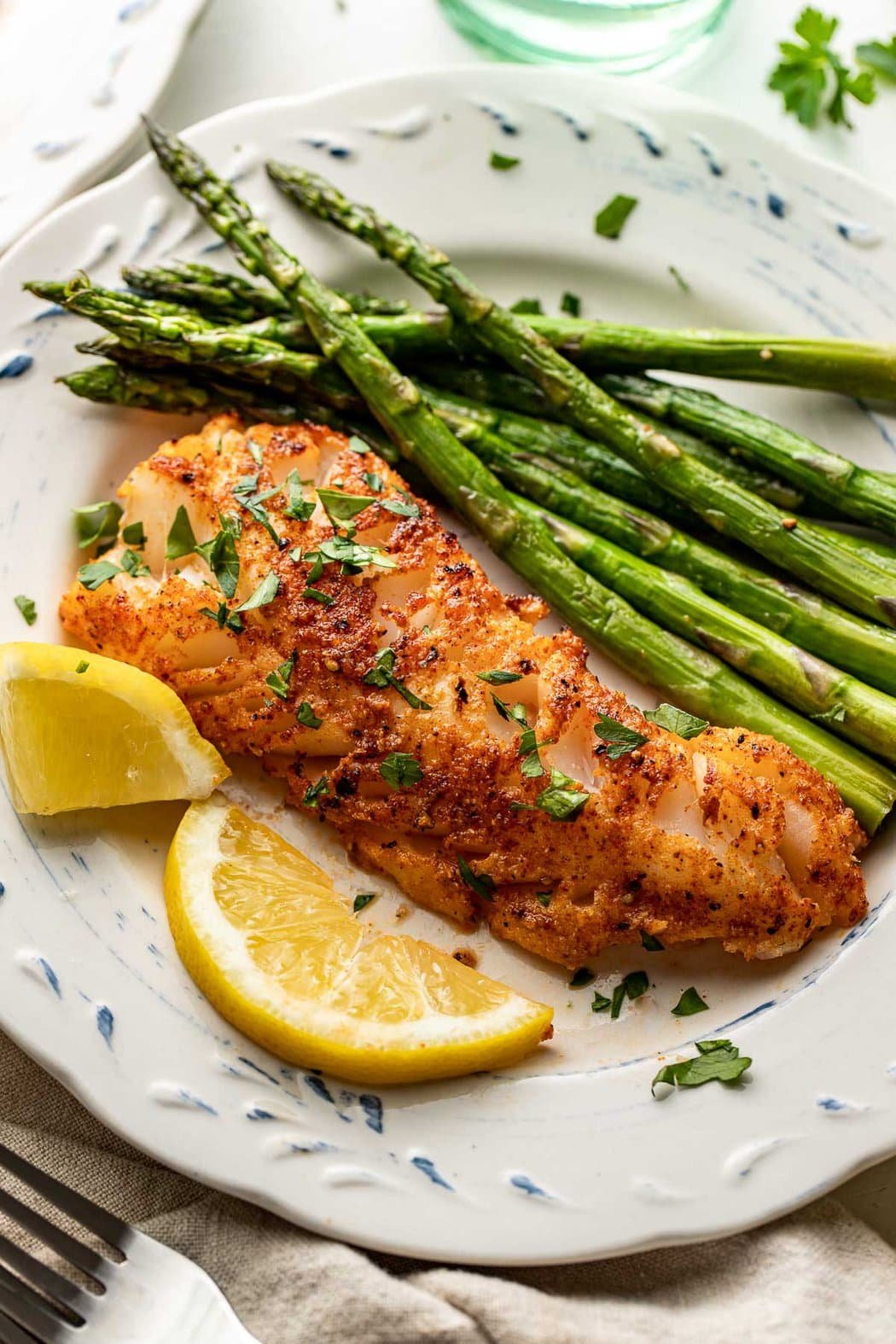 Close up view of a plate of Air Fryer Cod with a side of asparagus and lemon wedges on the side.