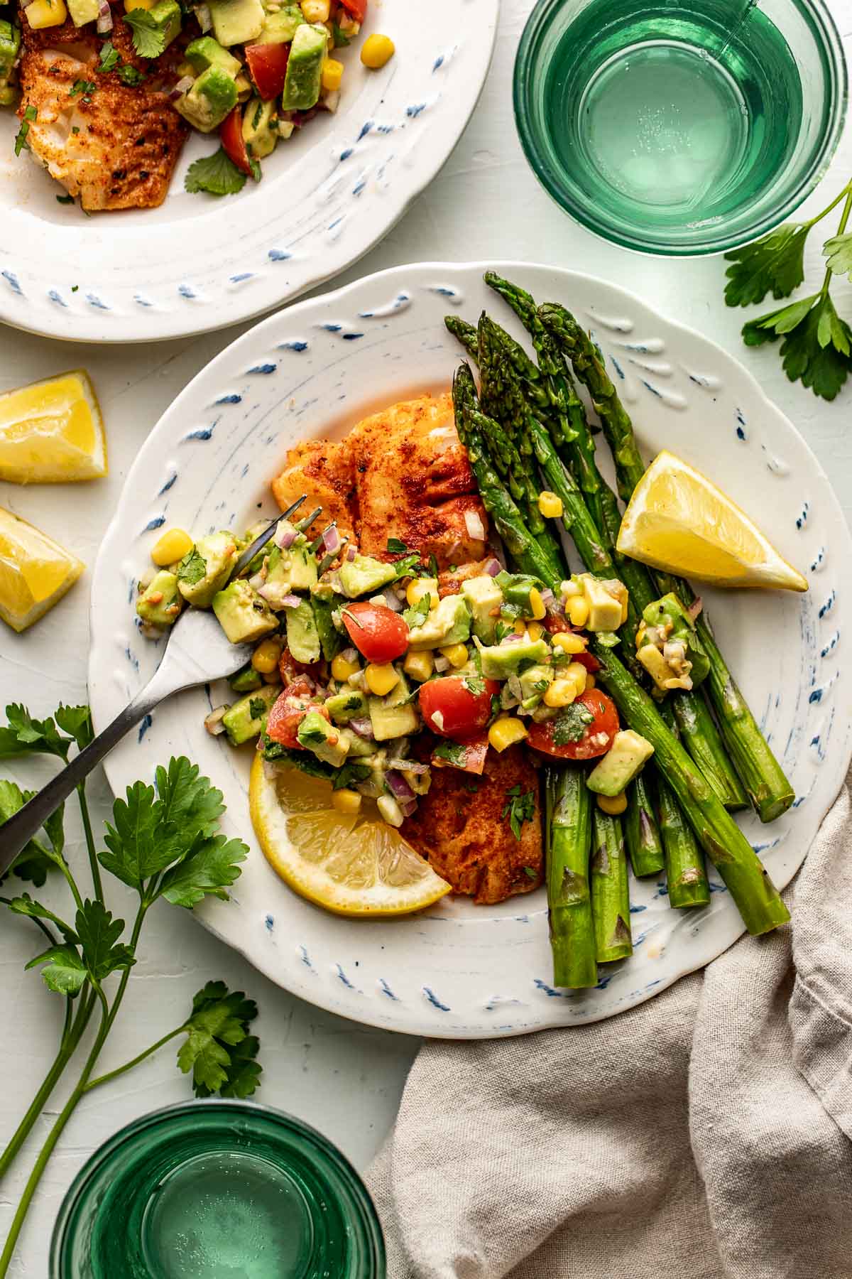 Overhead view of a plate of Air Fryer Cod topped with fresh avocado salsa and a side of asparagus.
