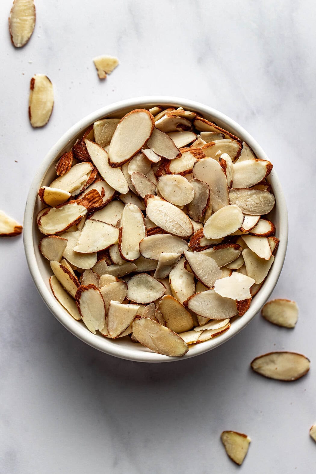 Close up view of a bowl of thinly sliced almonds in a white bowl.