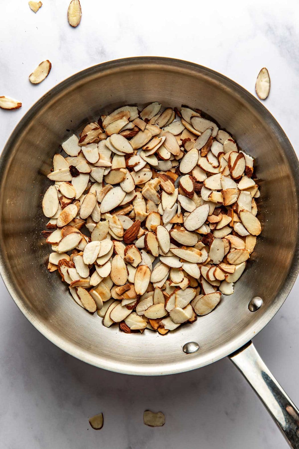 Overhead view of a stainless-steel pan filled with toasted sliced almonds. 