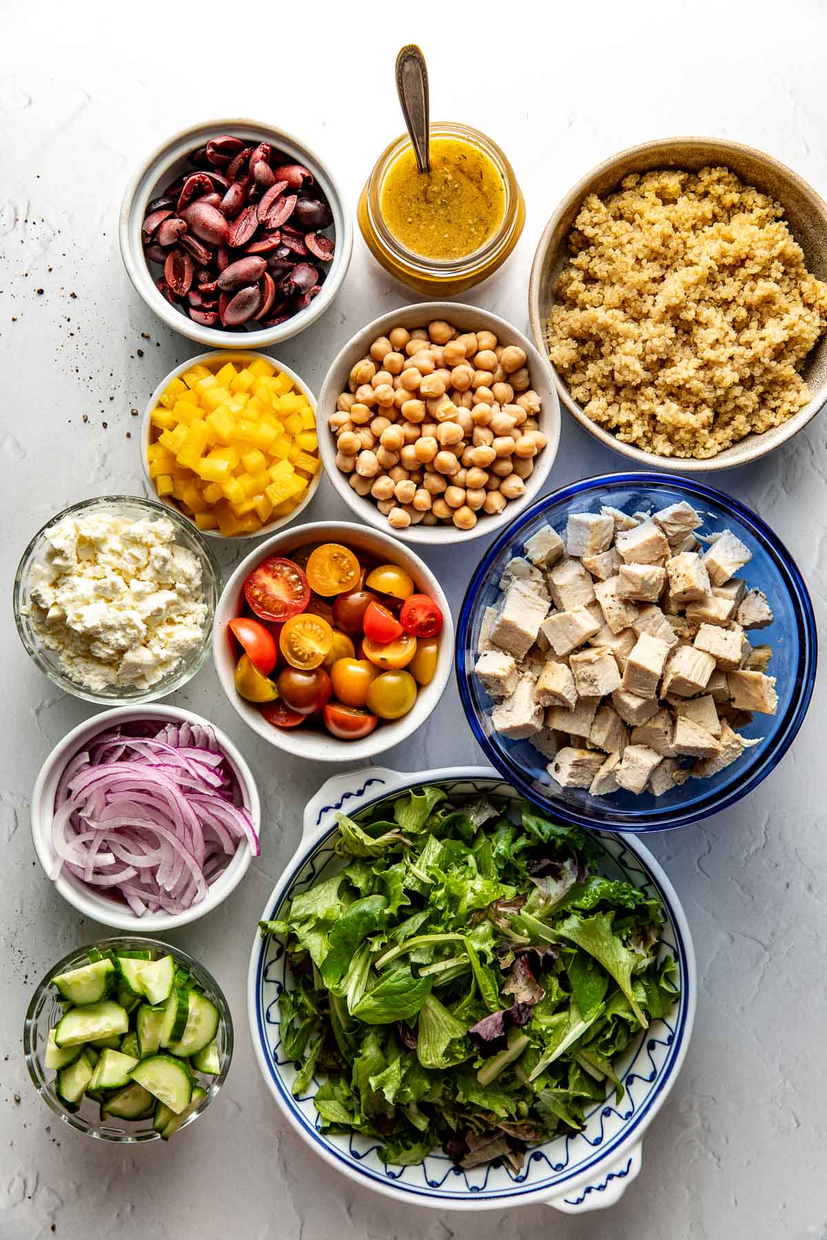 Overhead view of a variety of ingredients for Chopped Mediterranean Salad with Chicken in different sized bowls. 