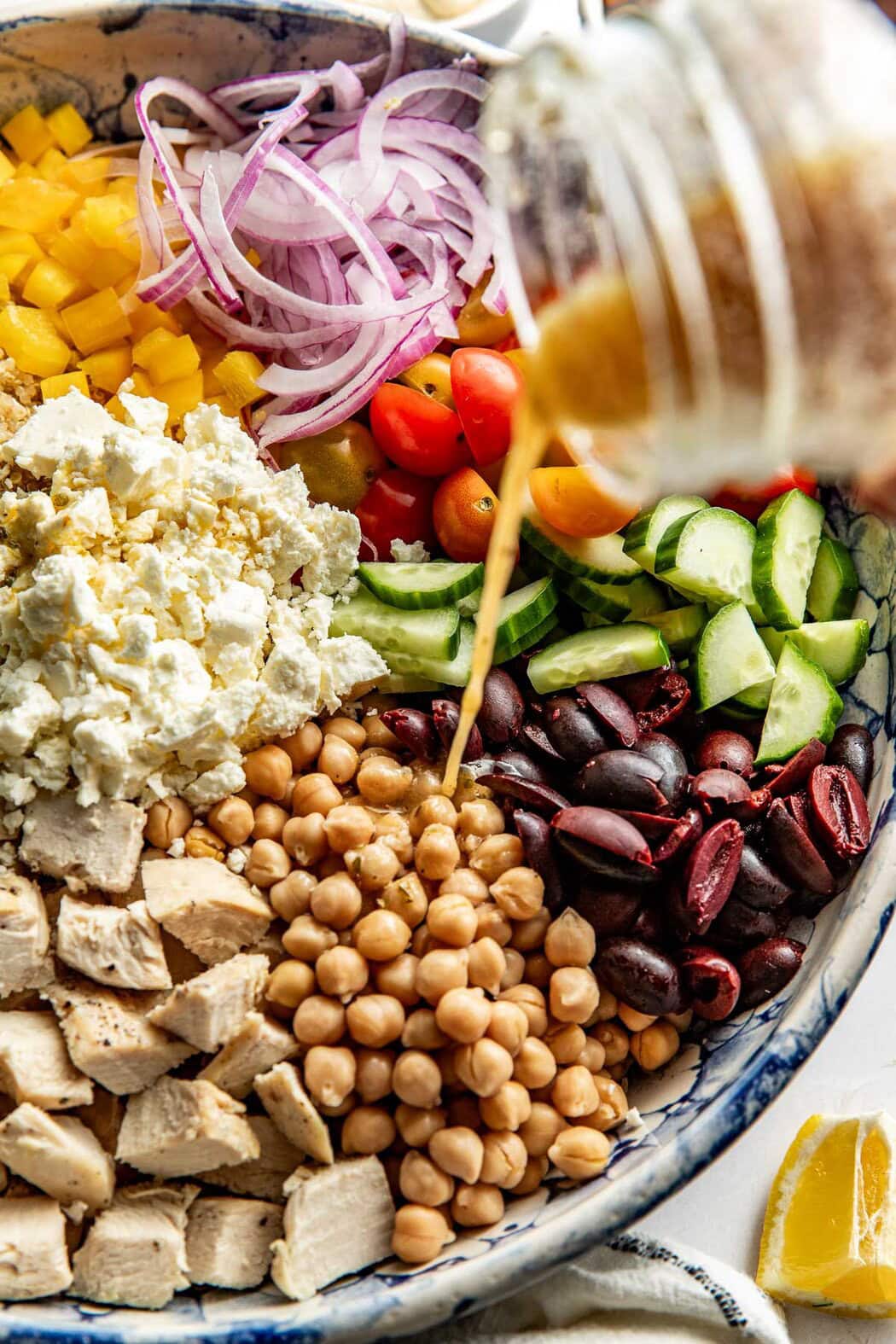 Close up view of a Chopped Mediterranean Salad with a mason jar of dressing pouring red wine vinaigrette over the ingredients. 