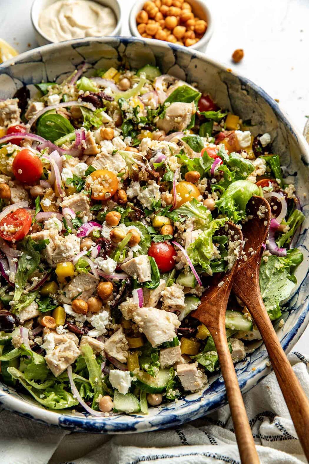 Close up view of a colorful bowl of Chopped Mediterranean Salad with Chicken and 2 wooden spoons in the bowl. 