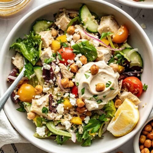 Overhead view of a white bowl of Chopped Mediterranean Salad with Chicken topped with a dollop of hummus.