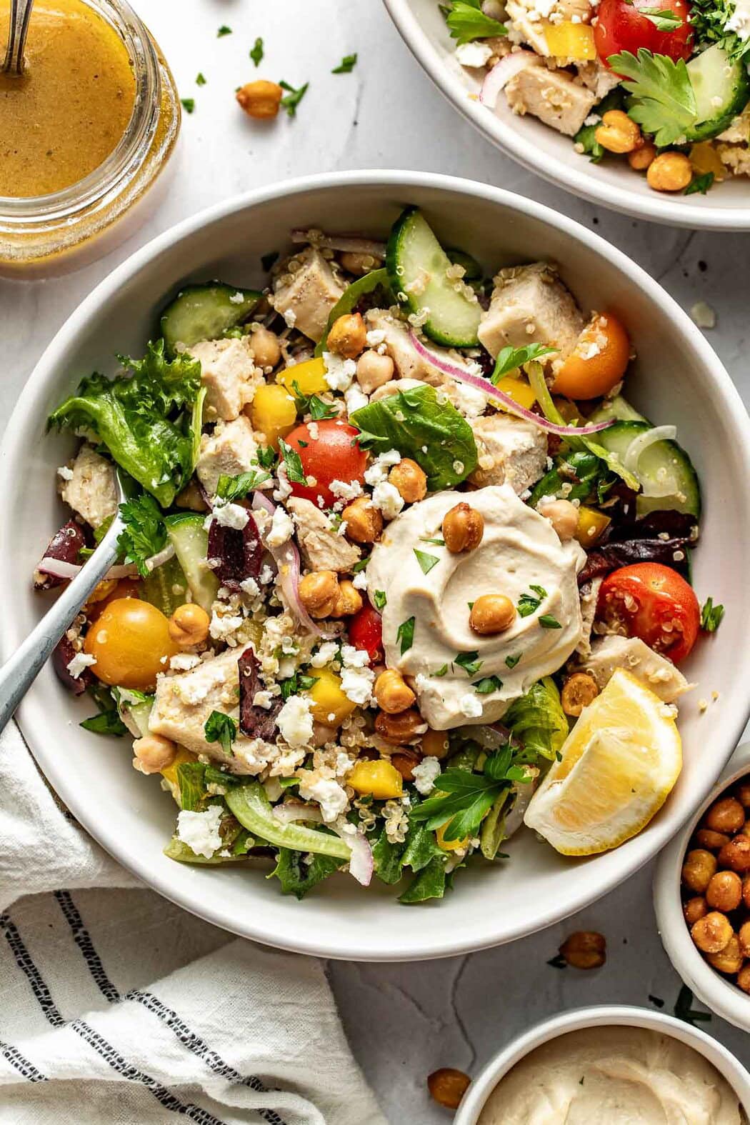 Overhead view of a colorful bowl of Chopped Mediterranean Salad with Chicken and a dollop of hummus with a garnish of lemon on the side. 