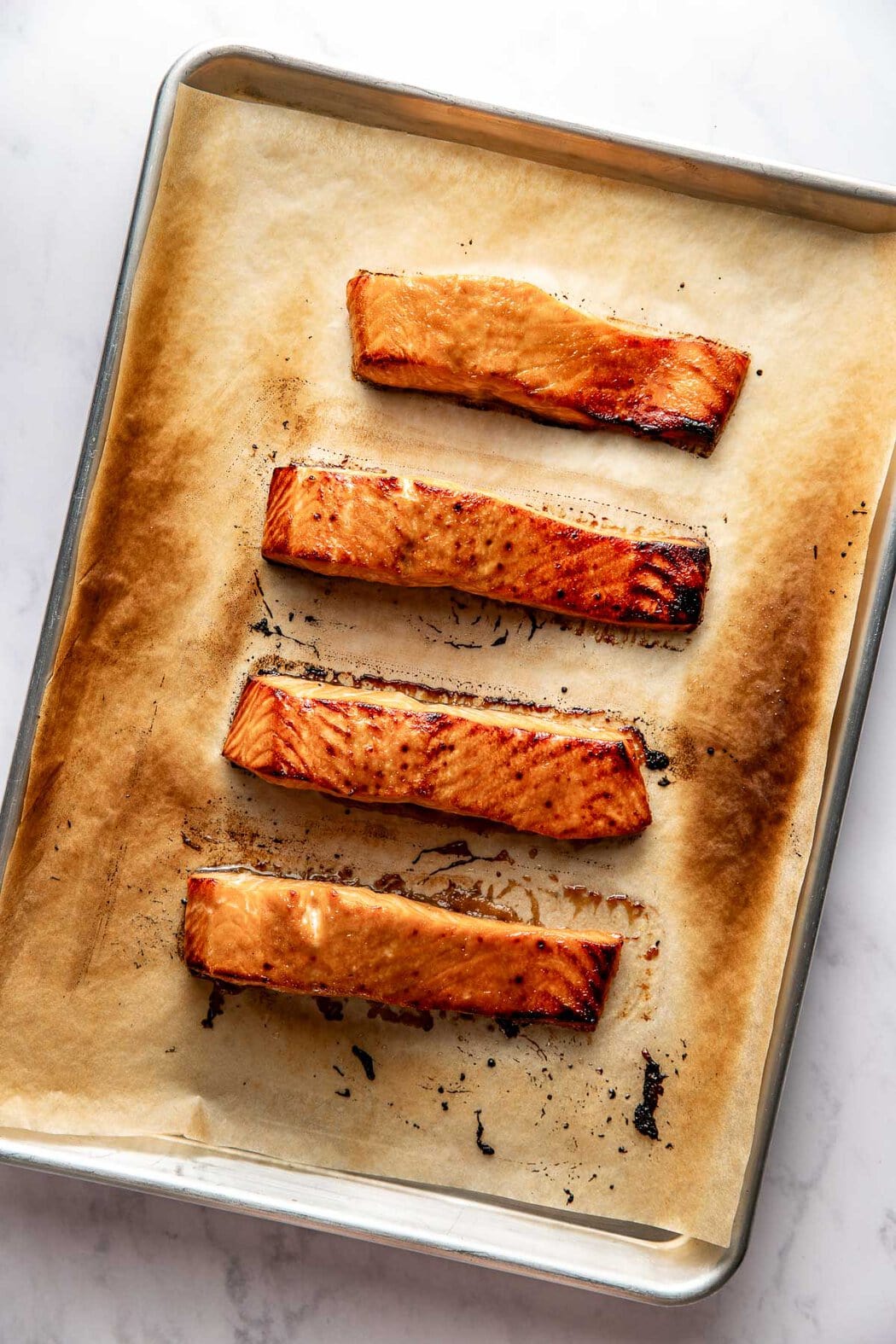Overhead view of a baking sheet filled with crisp Miso-Glazed Salmon fillets on parchment paper. 