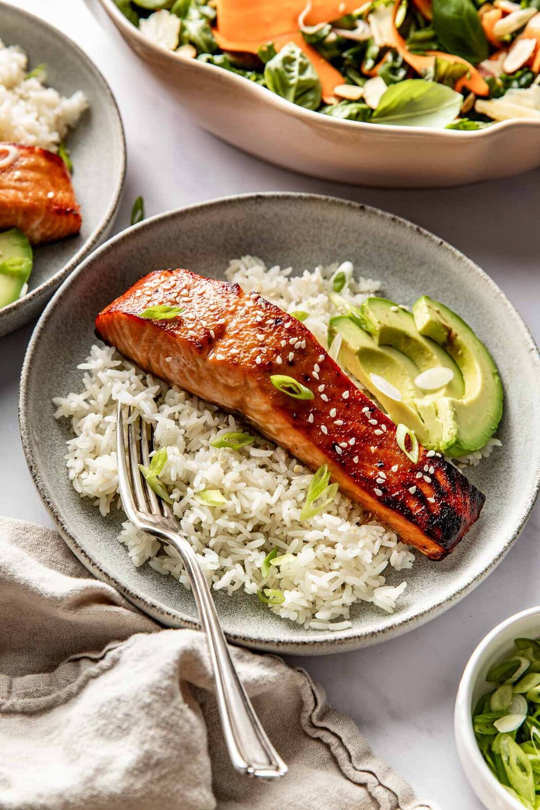 Overhead view of a ceramic plate filled with white rice and Miso-Glazed Salmon with sesame seeds and green onions on top.