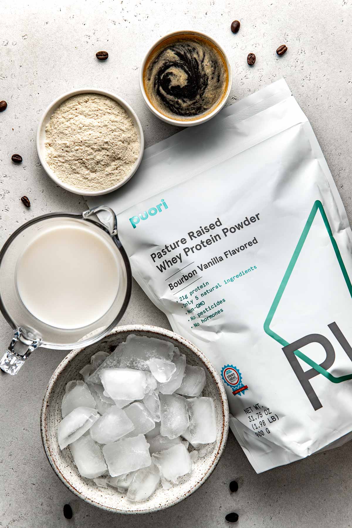 Overhead view of a bag of protein surrounded by Protein Coffee ingredients in different sized bowls. 