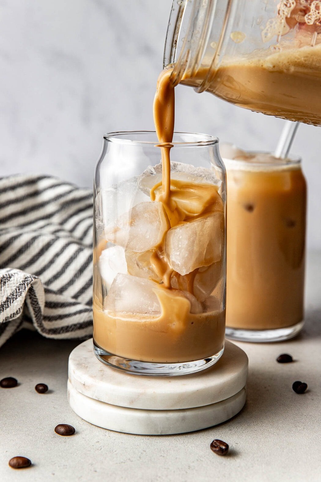 Close up view of a mason jar pouring Protein Coffee into a glass of ice. 