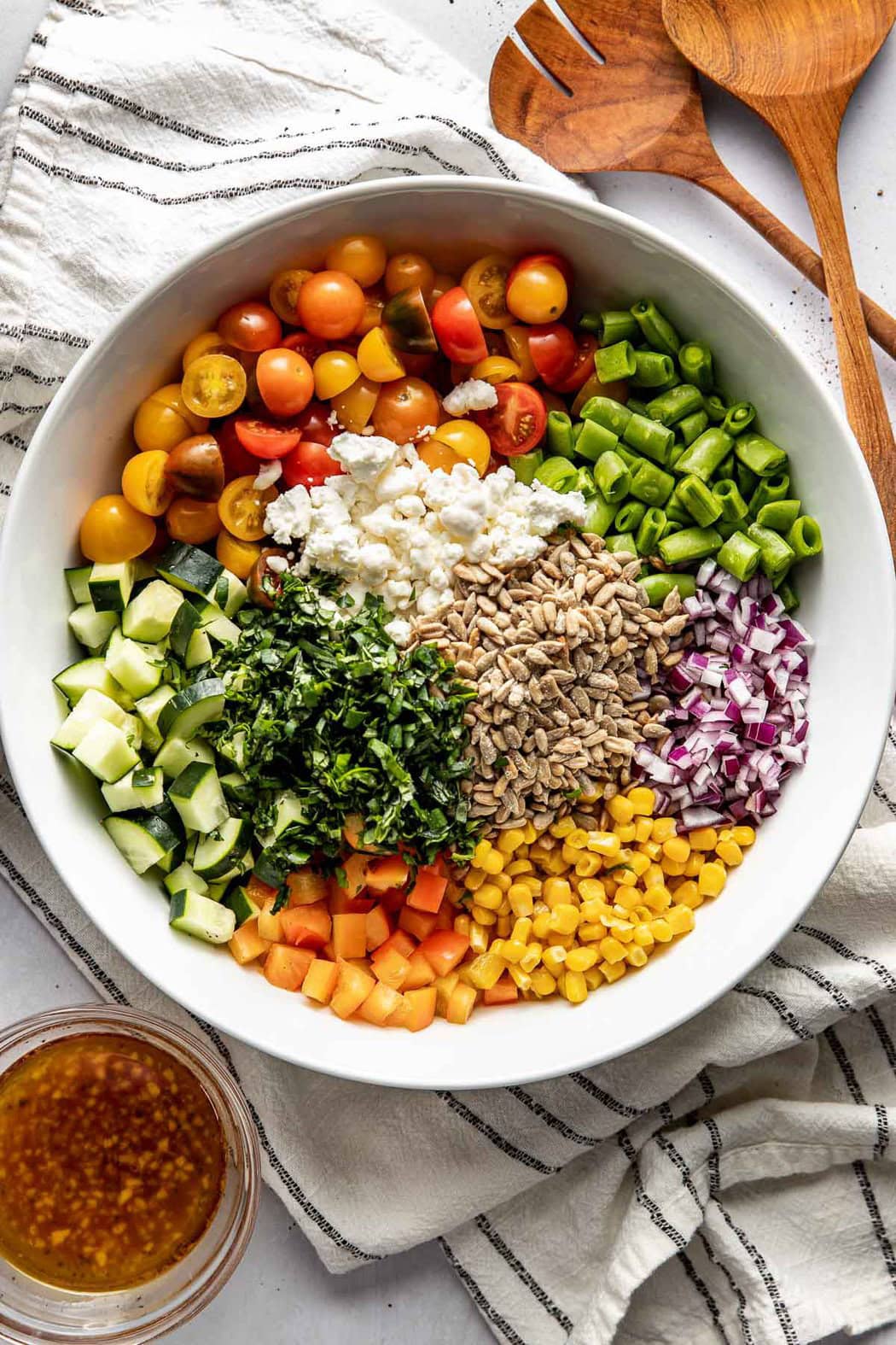 Overhead view of a bowl filled with colorful summer salad ingredients in different sections of the bowl ready for stirring. 
