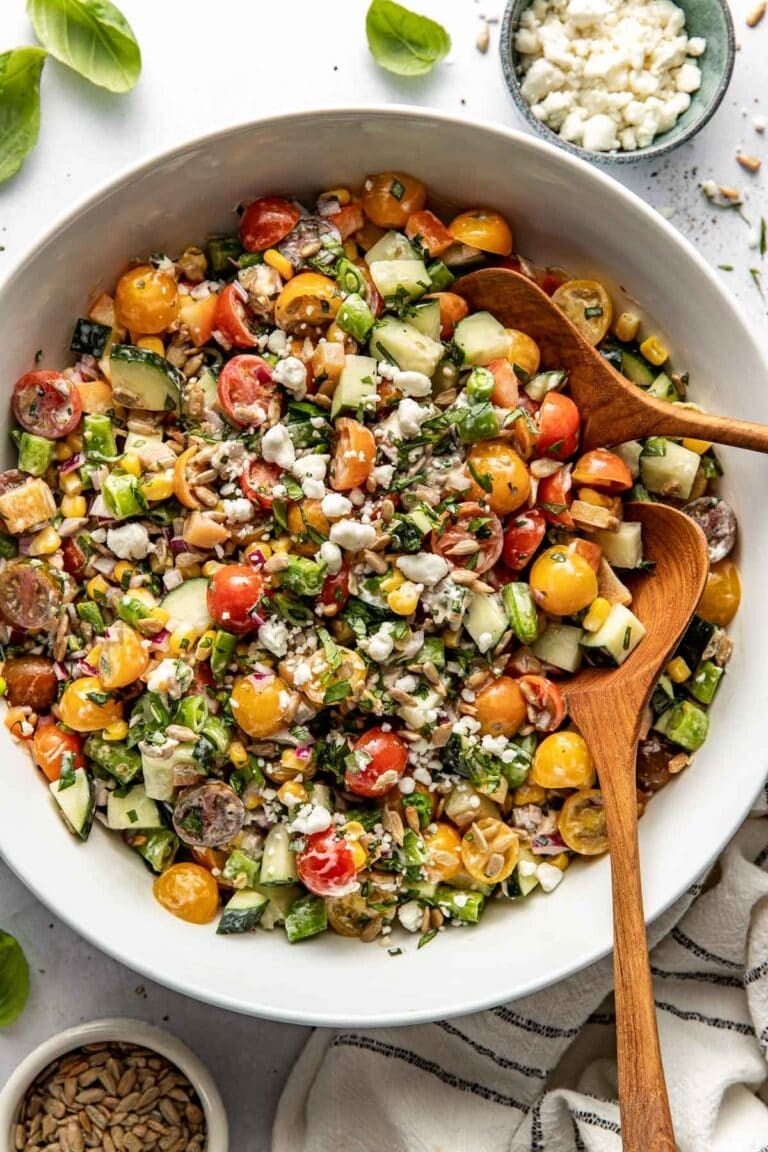 Overhead view of a bowl of summer salad topped with fresh herbs and crunchy sunflower seeds.