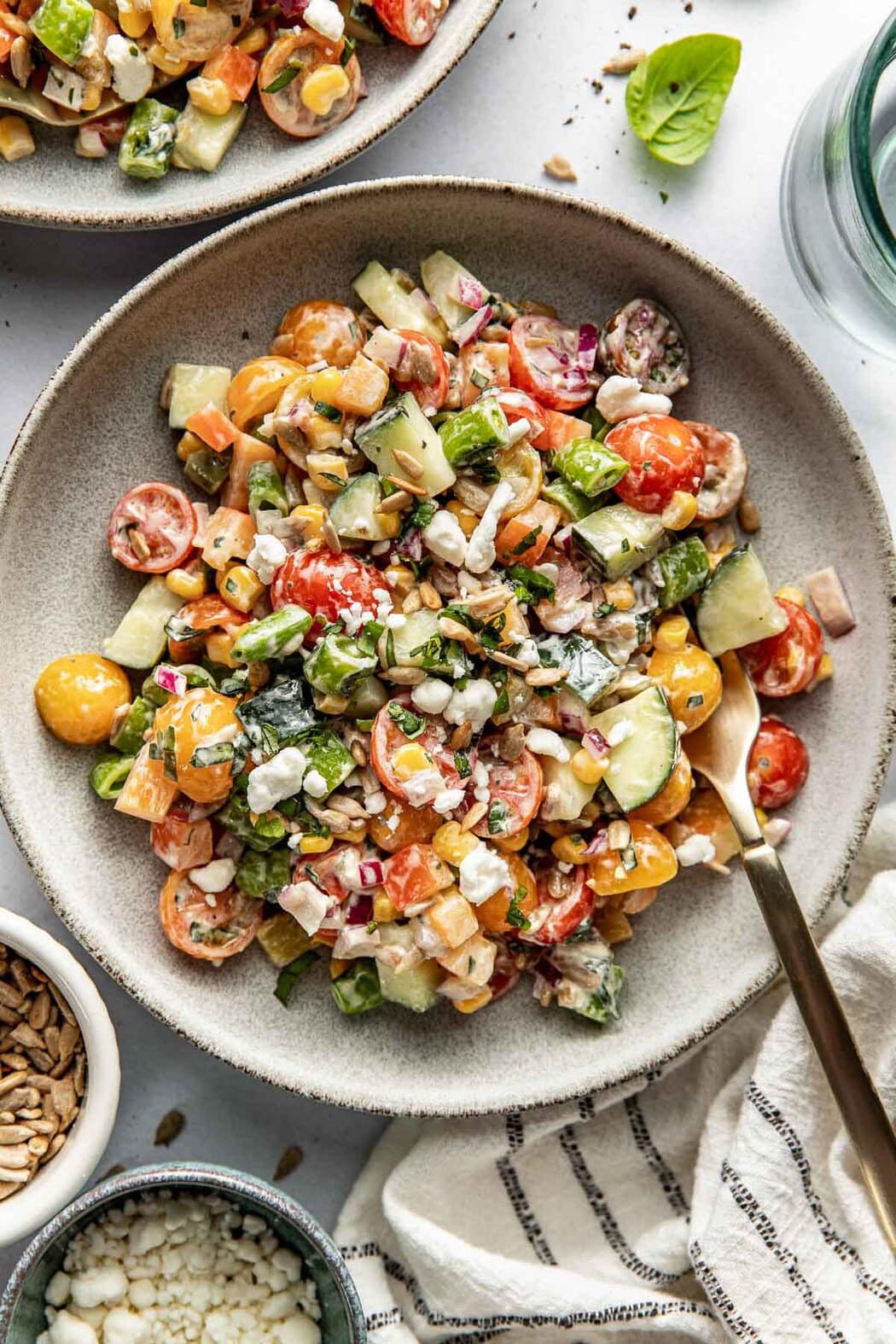 Close up view of a bowl of fresh colorful summer salad topped with crunchy sunflower seeds and goat cheese crumbles.