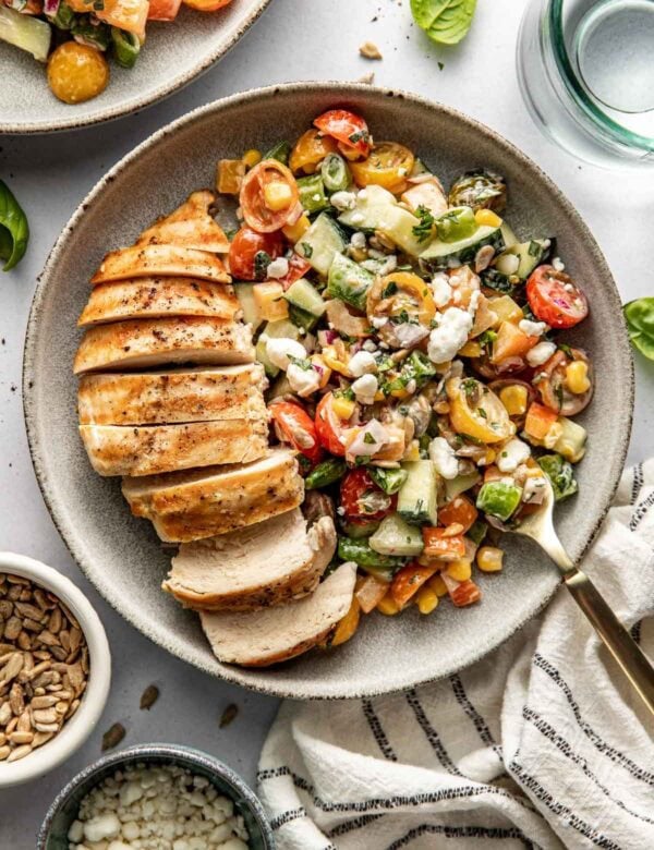 Overhead view white bowl filled with summer veggies and grilled sliced chicken breast.