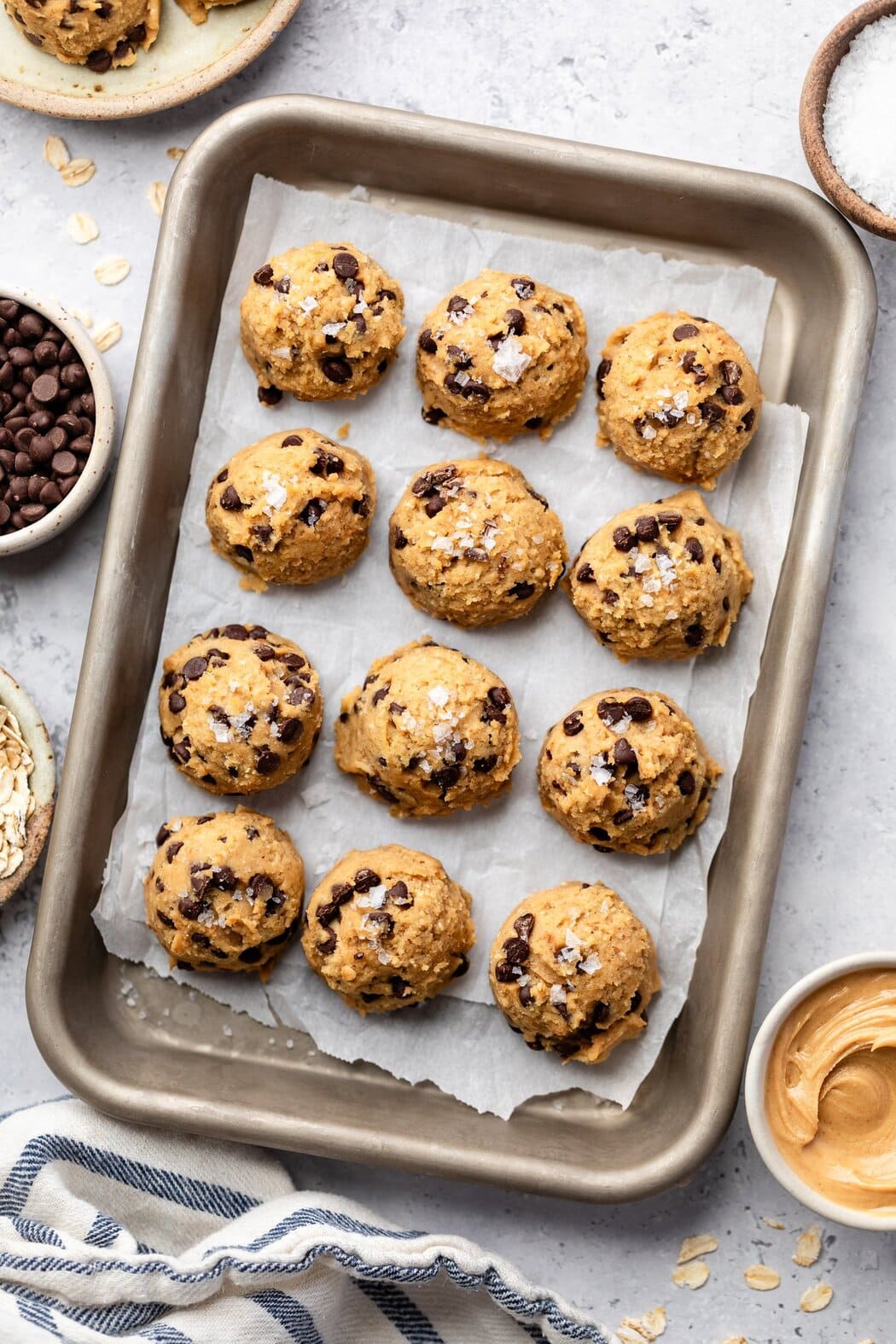 Close up view of a sheet pan of Chickpea Cookie Dough balls topped with chocolate chips and flakey sea salt.