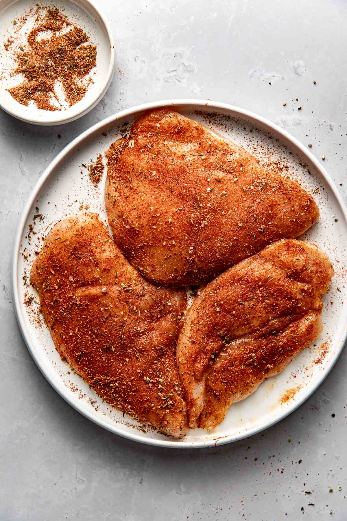 Overhead view of a plate of three chicken breasts seasoned and ready for cooking. 