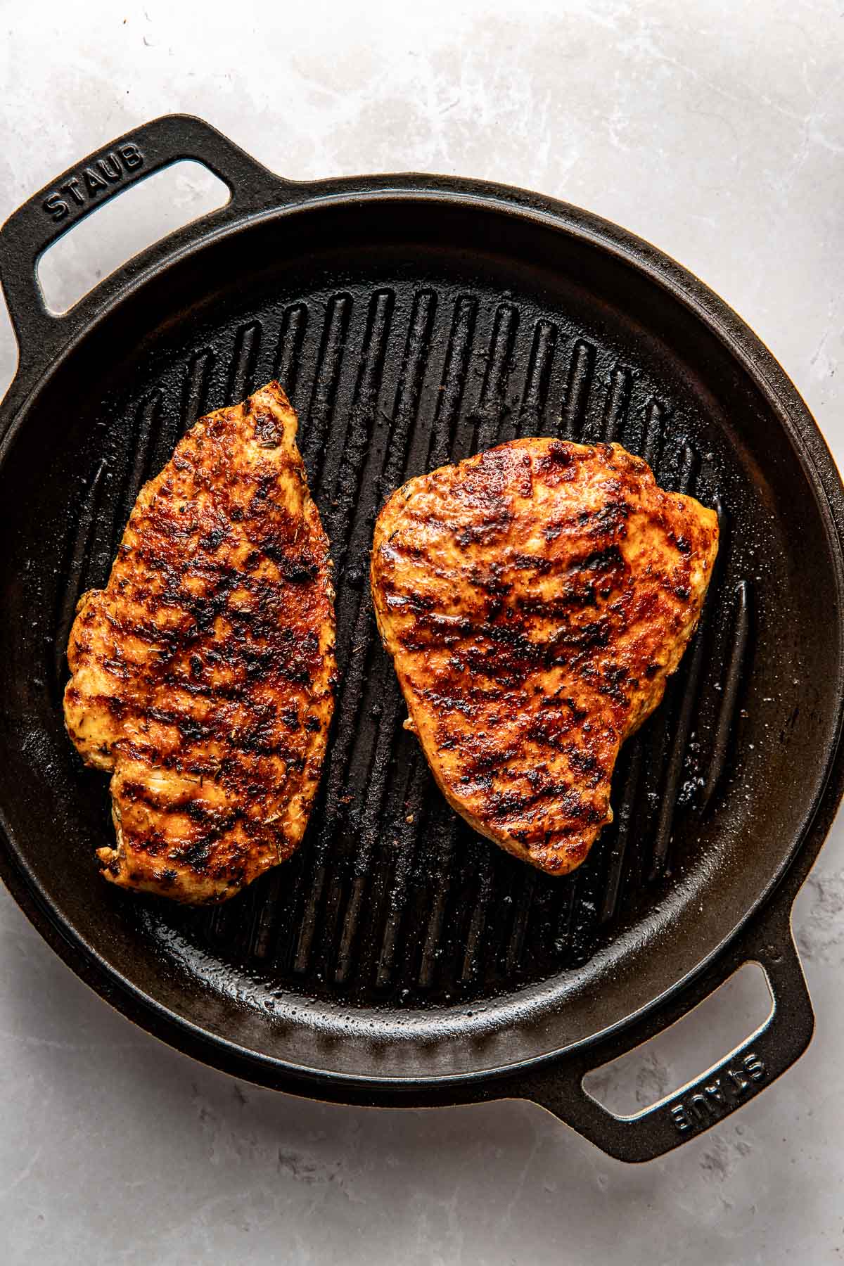 Overhead view of a cast iron grill pan with two blacked chicken breasts on it with crisp grill marks. 