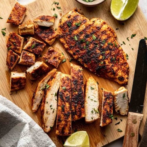 Overhead view of a wooden cutting board filled with Blackened Chicken pieces and lime wedges surrounding the board.