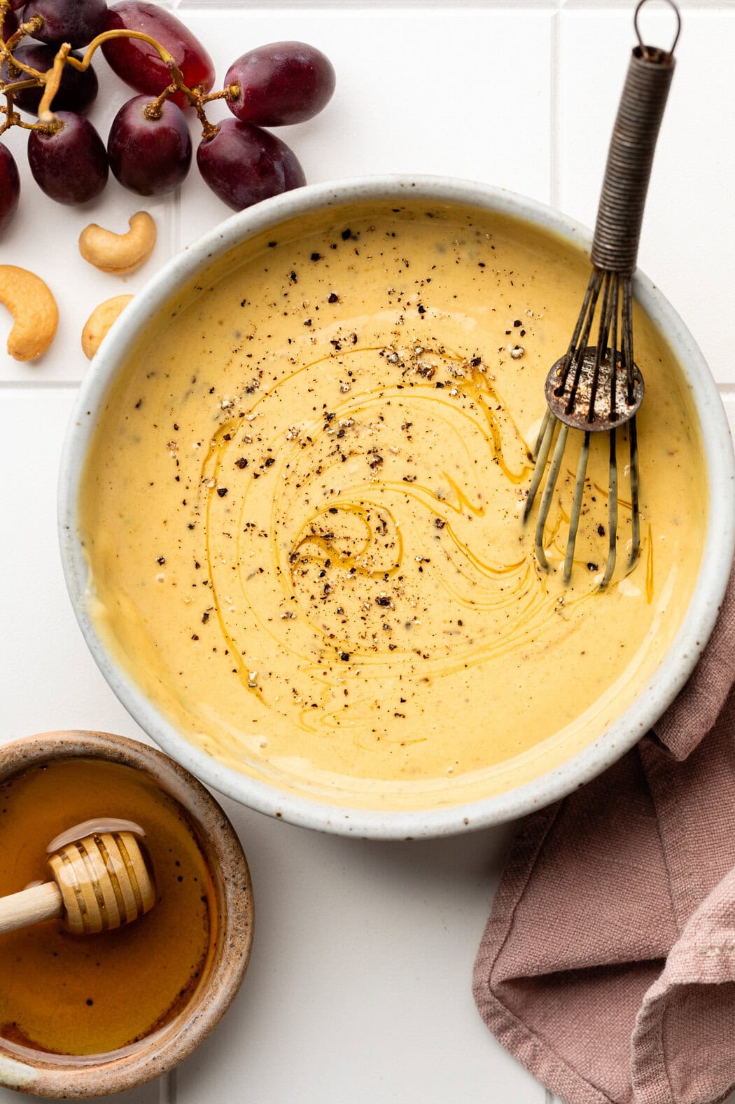 Overhead view of a bowl of honey mustard sauce with a whisk in the bowl topped with black pepper