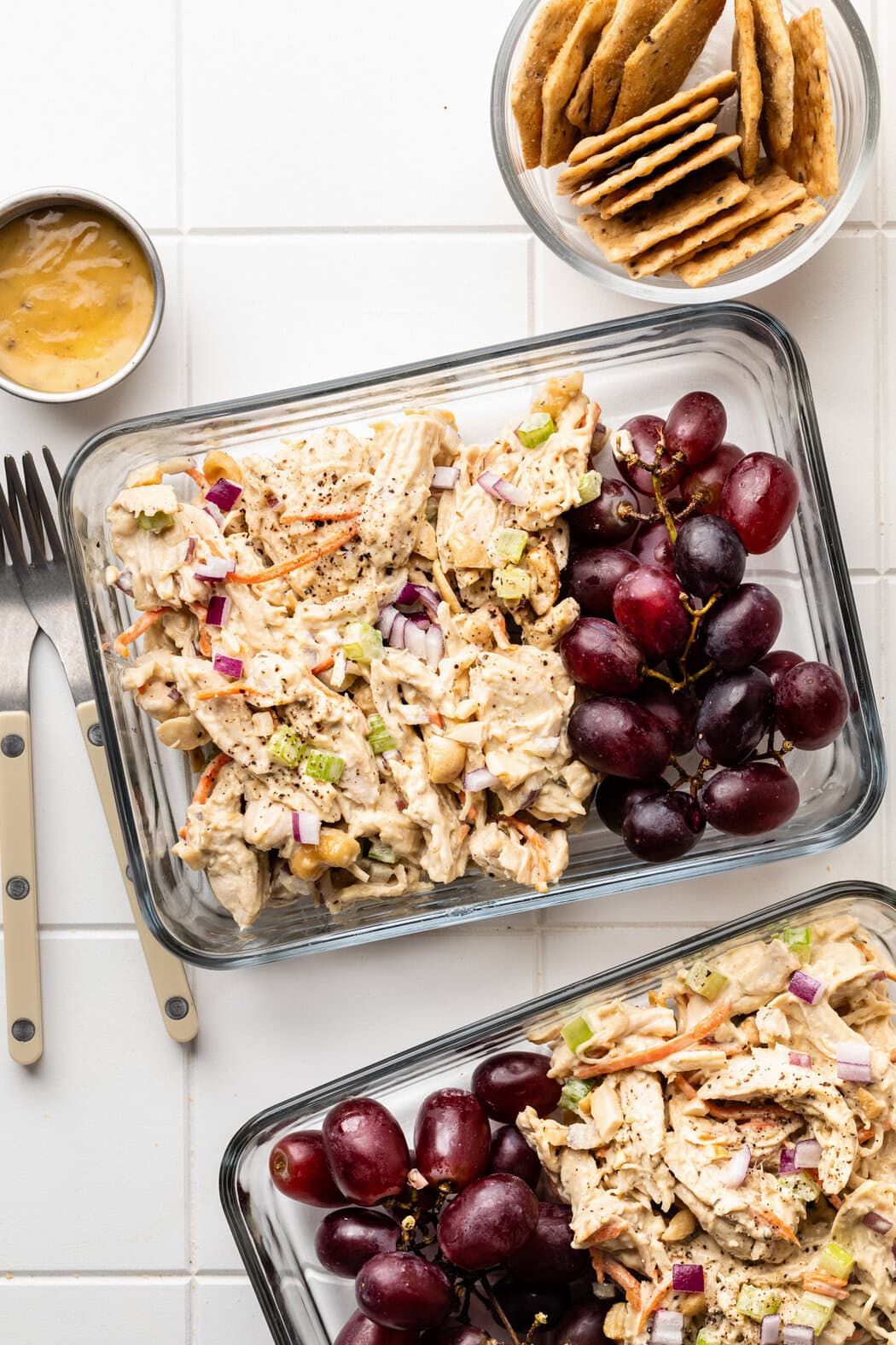 Overhead view of two glass rectangular meal prep containers filled with Honey Mustard Chicken Salad and purple grapes on the side.
