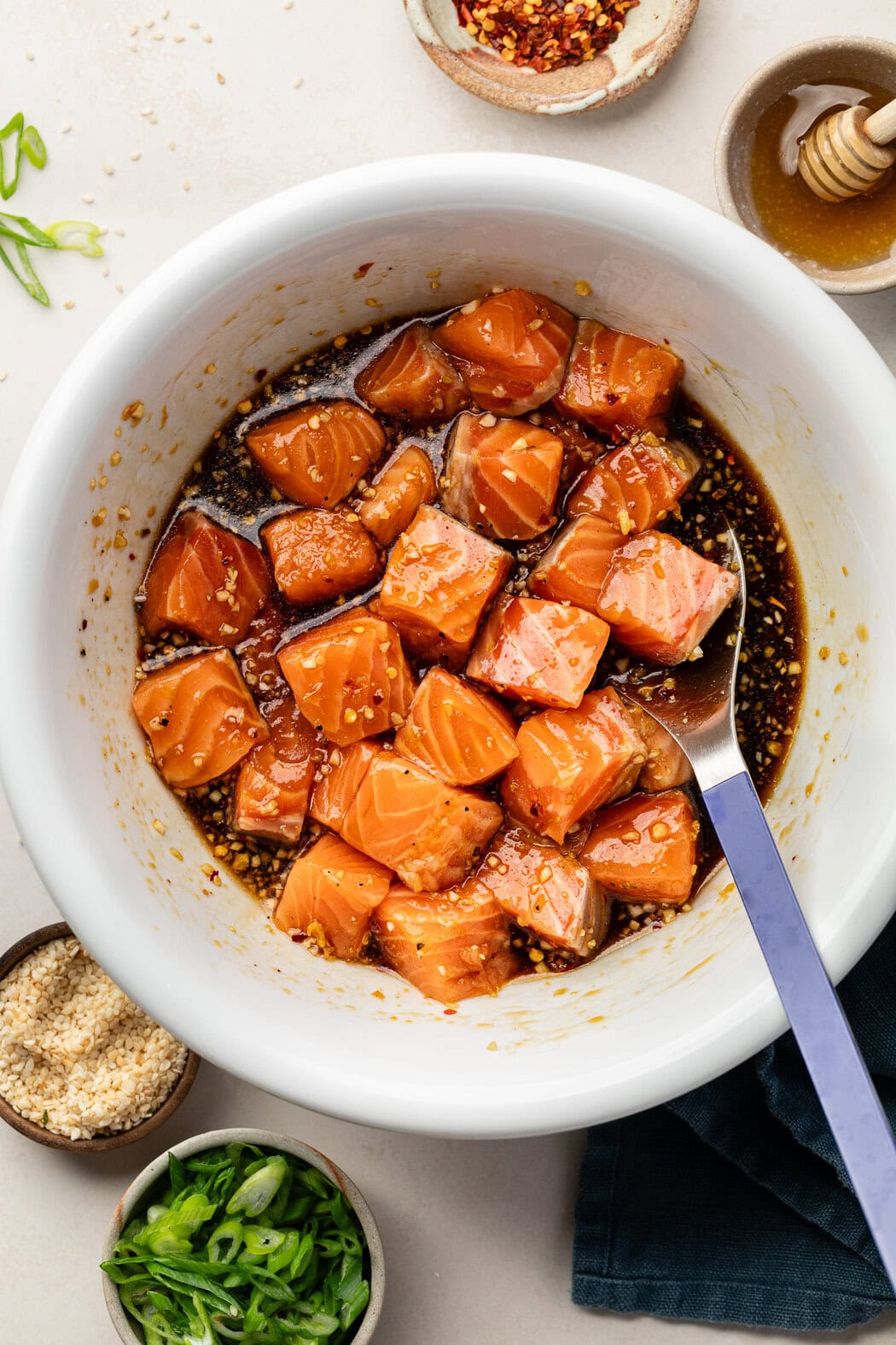 Overhead view of a white bowl of marinating salmon in 1-inch cubes. 