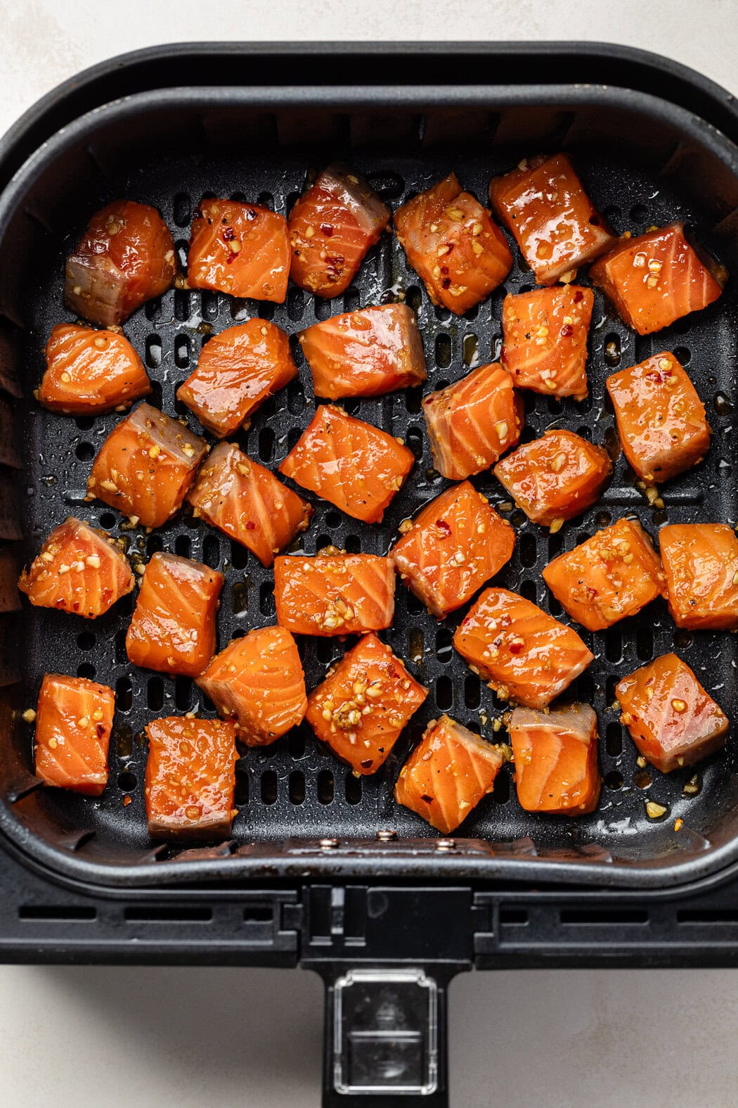 Overhead view of an air fryer basket filled with marinated salmon cubes ready for baking.