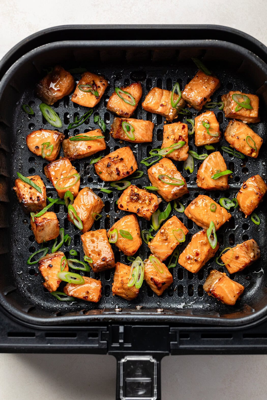 Overhead view of freshly baked Air Fryer Salmon Bites browned on the edges and topped with green onions.