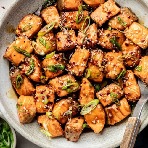 A white bowl of Air Fryer Salmon Bites topped with green onions and sesame seeds.