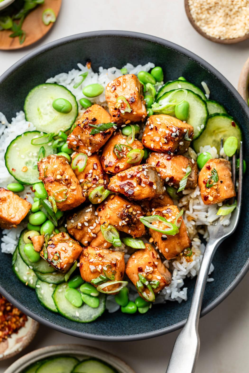 Close up view of a colorful Air Fryer Salmon rice bowl, filled with thinly sliced cucumbers, edamame beans, and sesame seeds. 