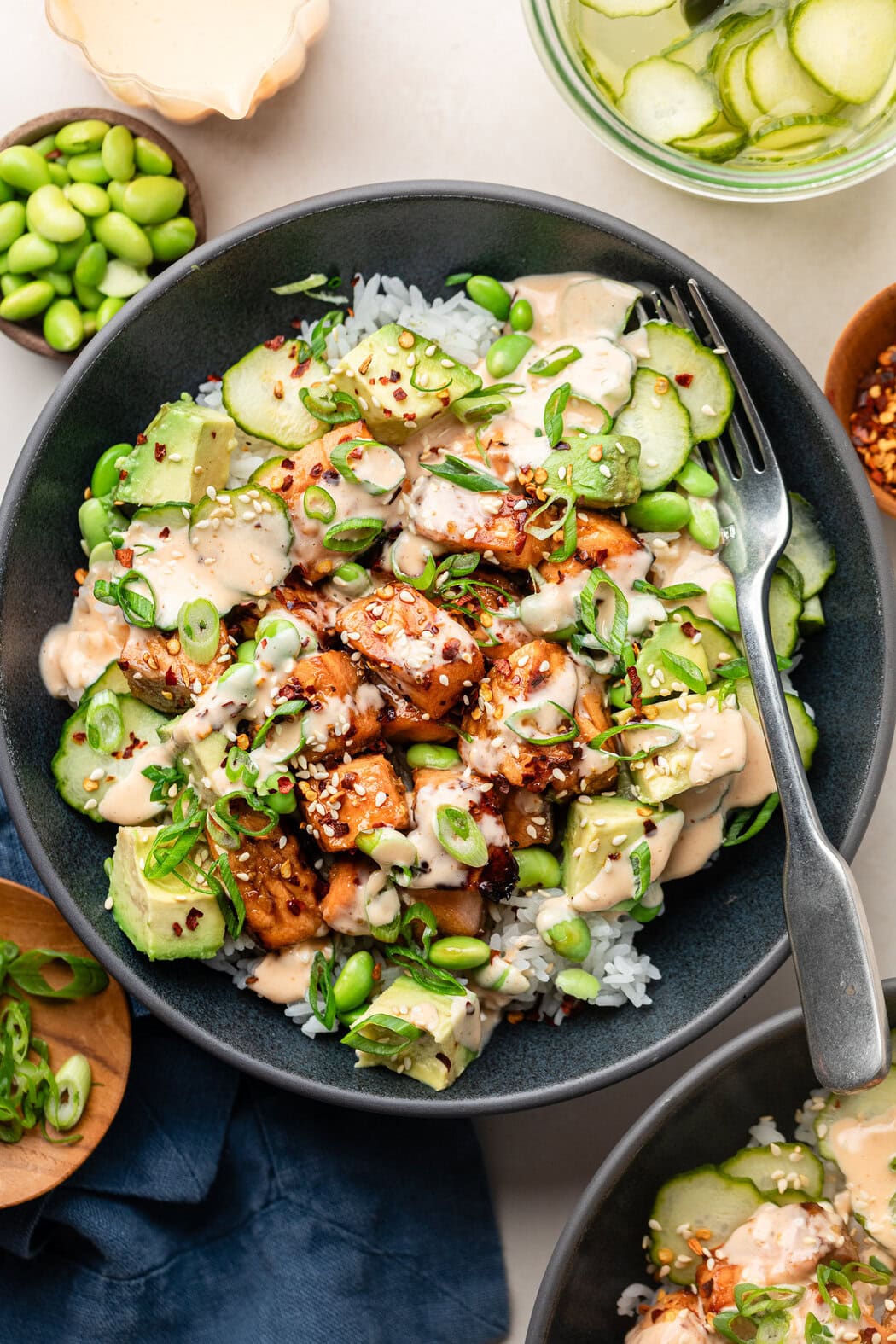 Overhead view of a plate of Air Fryer Salmon Bites on top of white rice, thinly sliced cucumbers and drizzled with a creamy sriracha sauce.