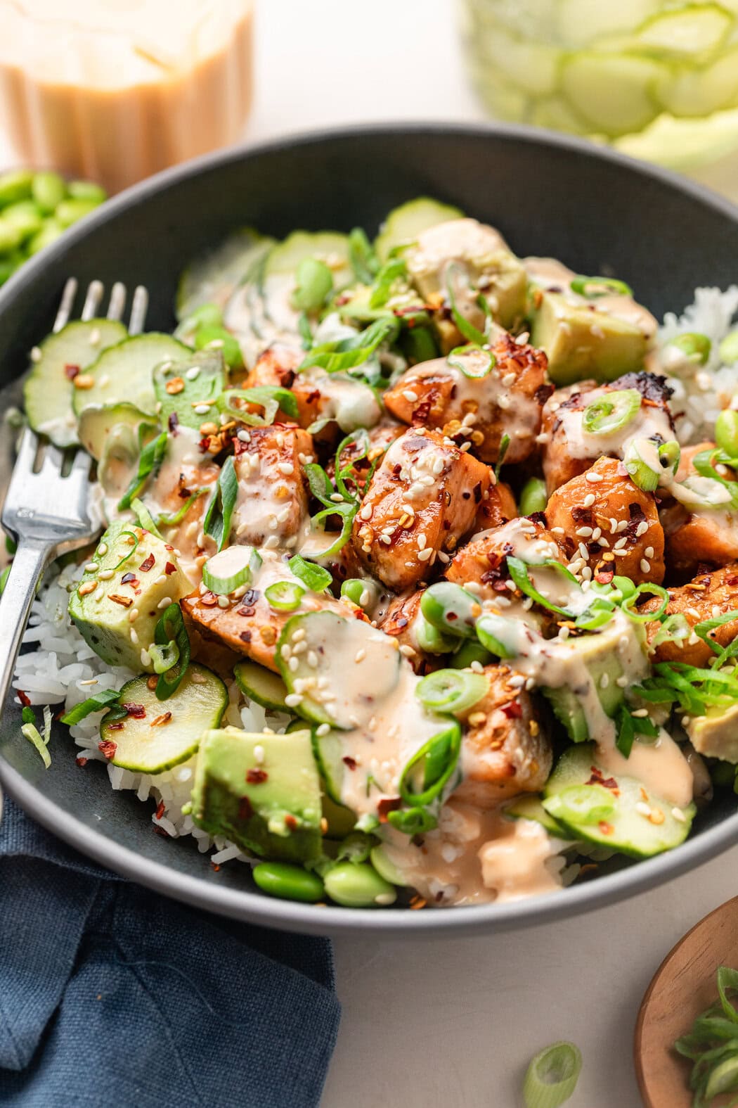 Close up view of a plate of Air Fryer Salmon Bites on top of white rice, and topped with green onions, sesame seeds, and drizzled with a creamy sriracha mayo sauce.