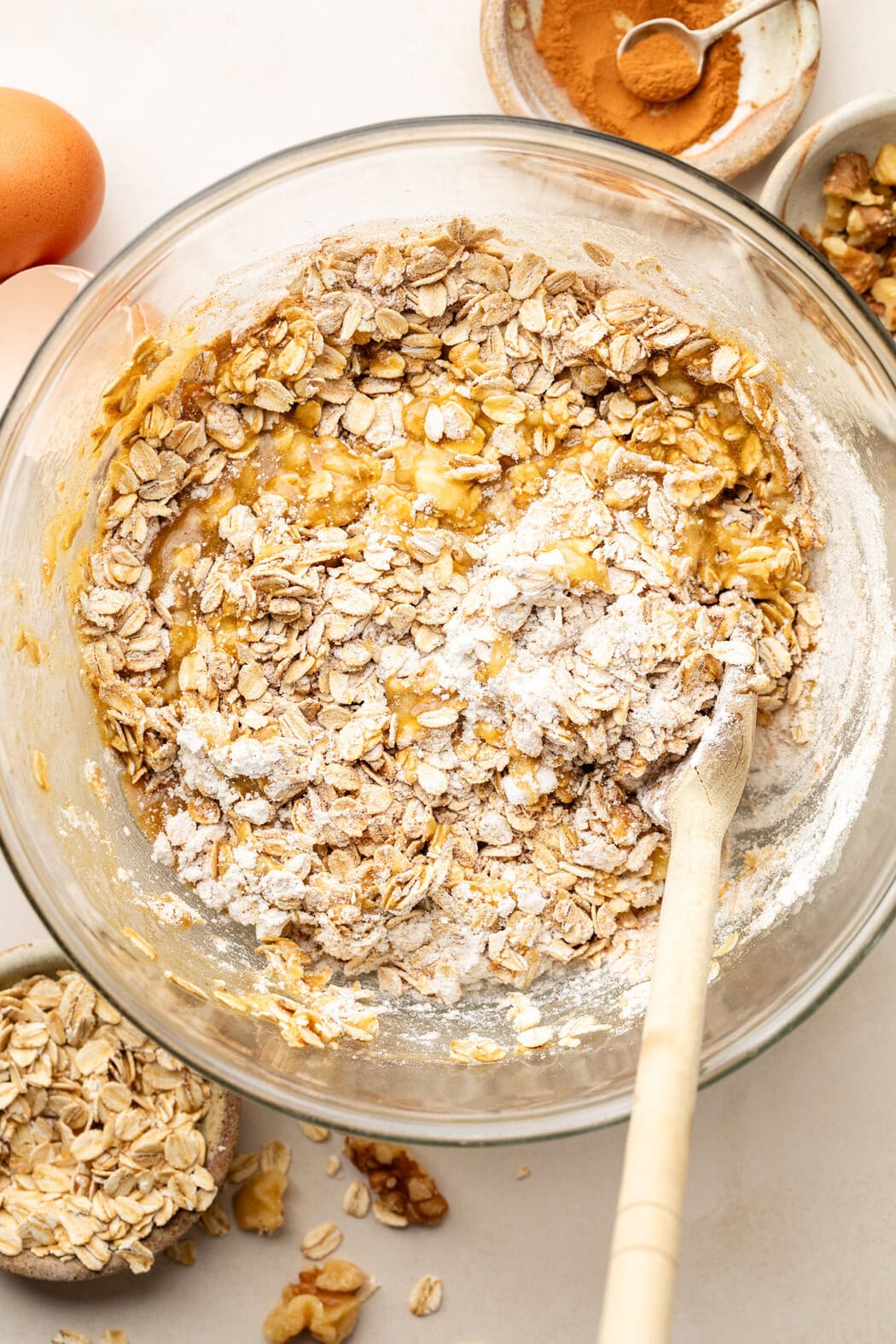 Overhead view of a glass bowl of Blueberry Oatmeal Breakfast Cookie batter being stirred with a wooden spoon. 